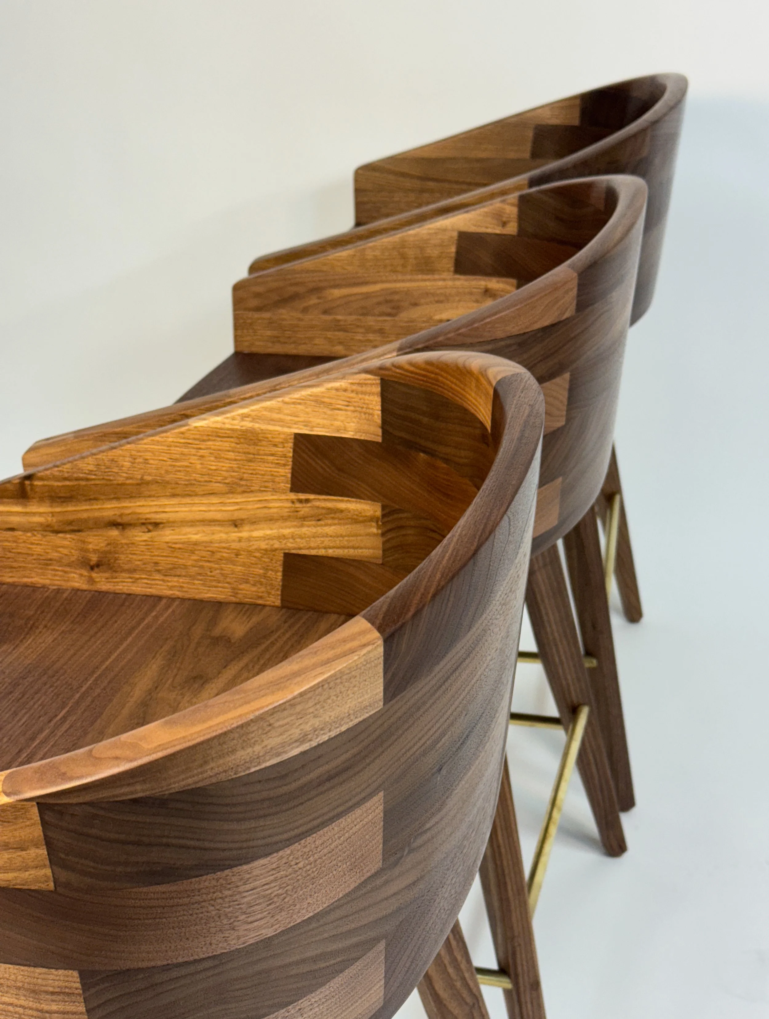 Three wooden chairs with curved backs and brass bars in a row.