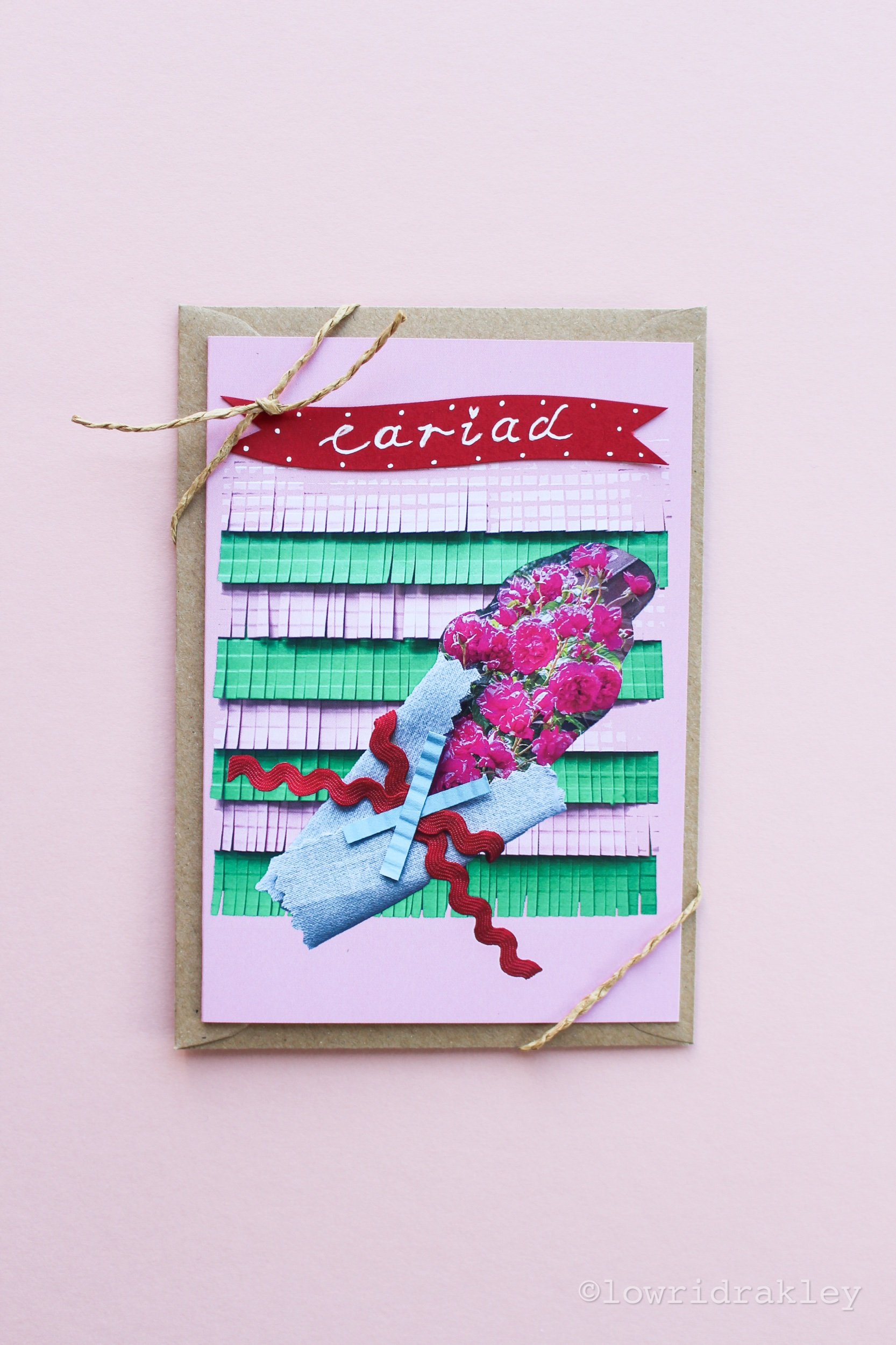 Handmade mixed-media greeting card featuring a vibrant pink rose bouquet collage on a fringed green and lilac background, topped with a red "Cariad" banner and tied with twine.