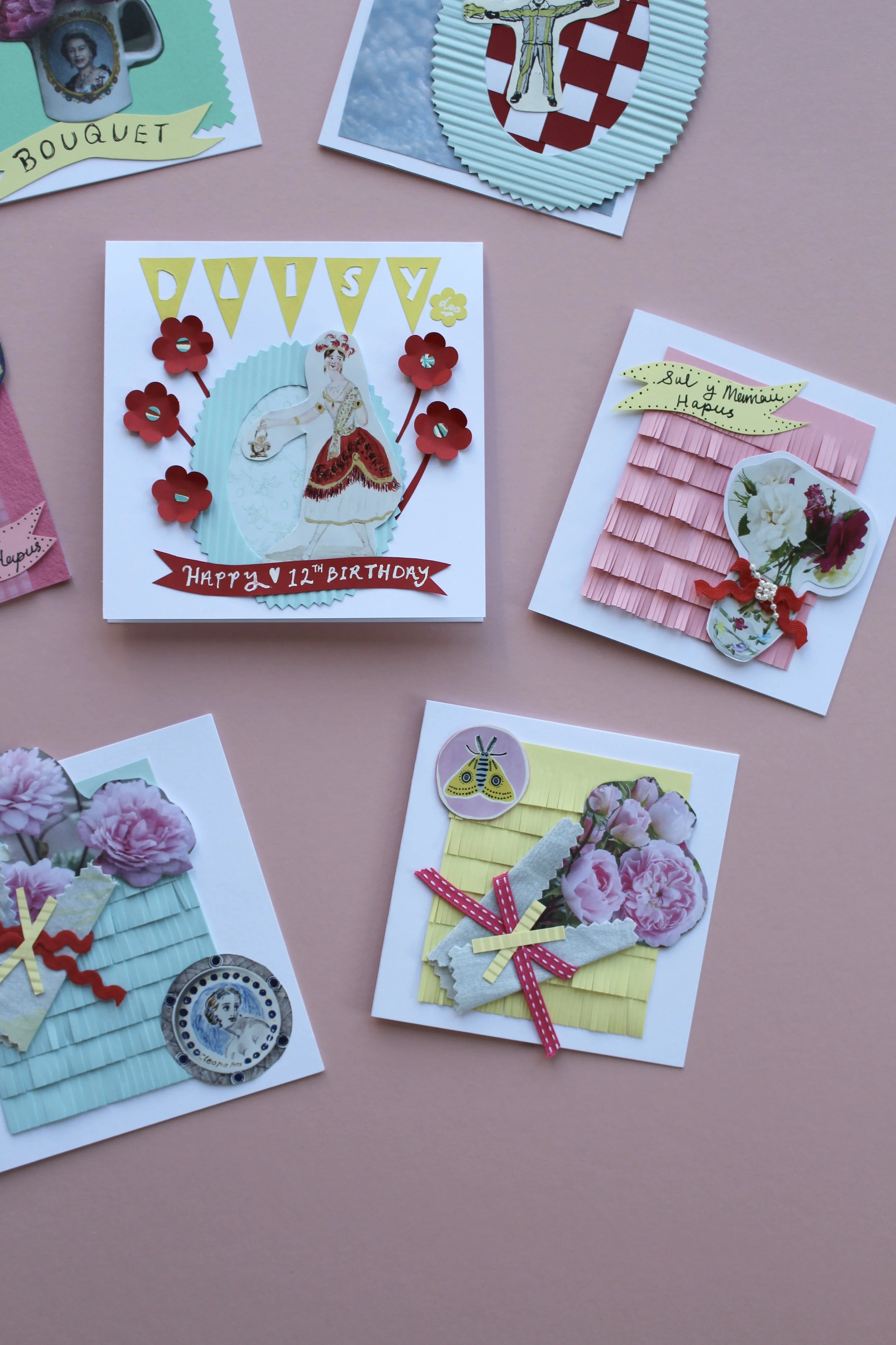 A collection of five handmade 3D greeting cards on a pink background, featuring intricate paper fringing, vintage-style floral collages.