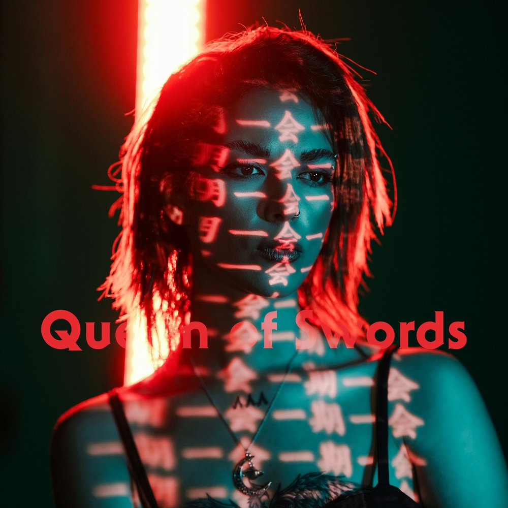 a sharp-eyed woman bathed in blue and red light stares forward as glowing kanji are projected across her face and chest. her expression is unreadable. she wears a moon pendant, framed by shadow.