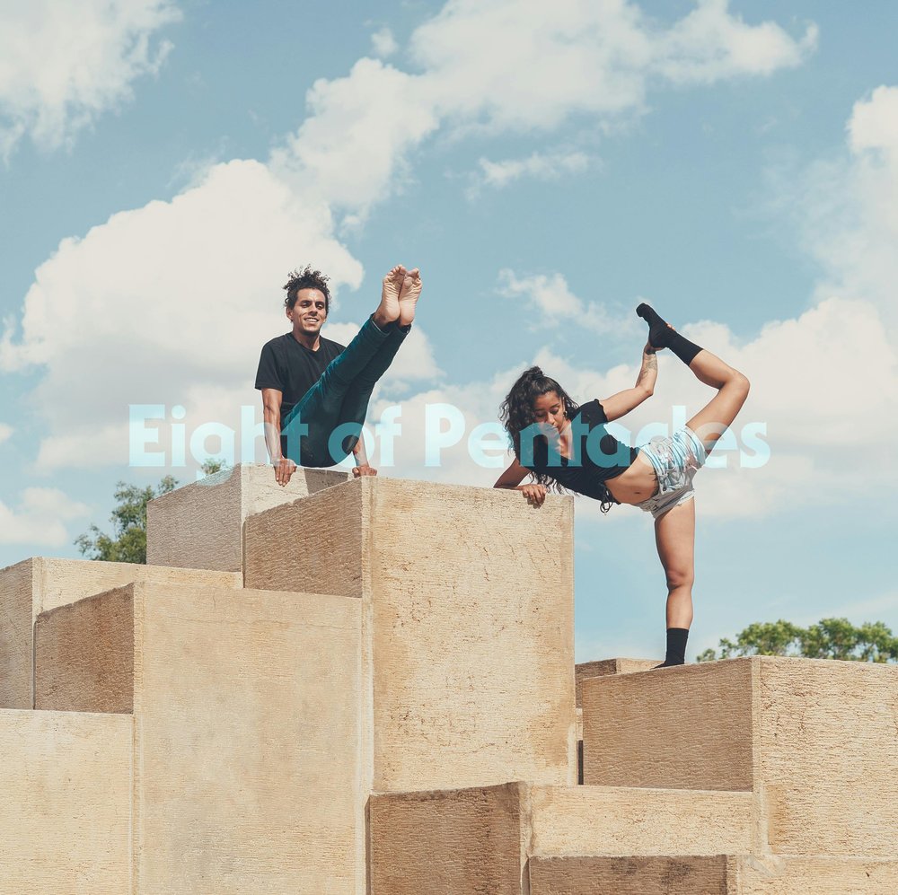 Two young people practice acrobatic poses atop large stone blocks. The sky is bright and blue. They look focused but joyful.