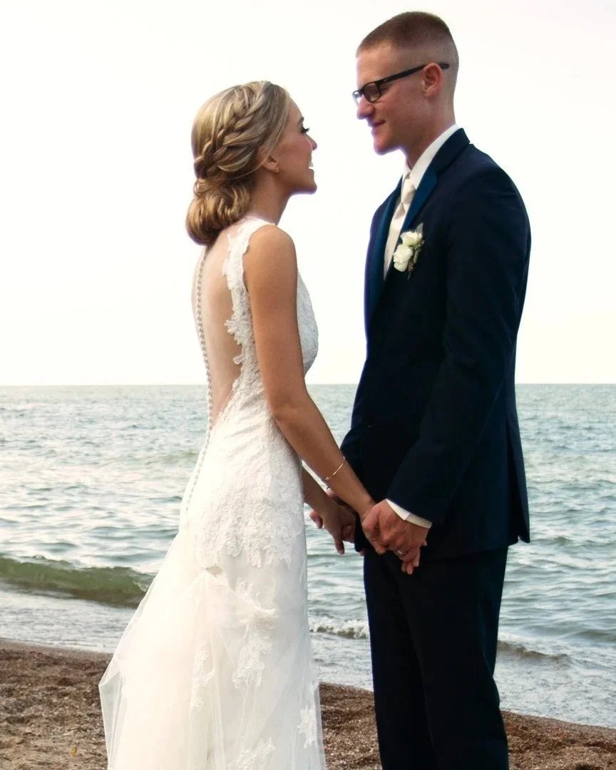 A bride and groom holding hands and facing each other on a beach,  on the shores of Lake Erie in Sandusky, Ohio.