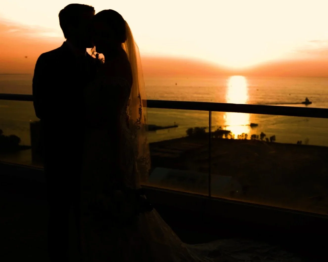 A silhouette of a wedding couple close together in Cleveland with a sunset over Lake Erie in the background.