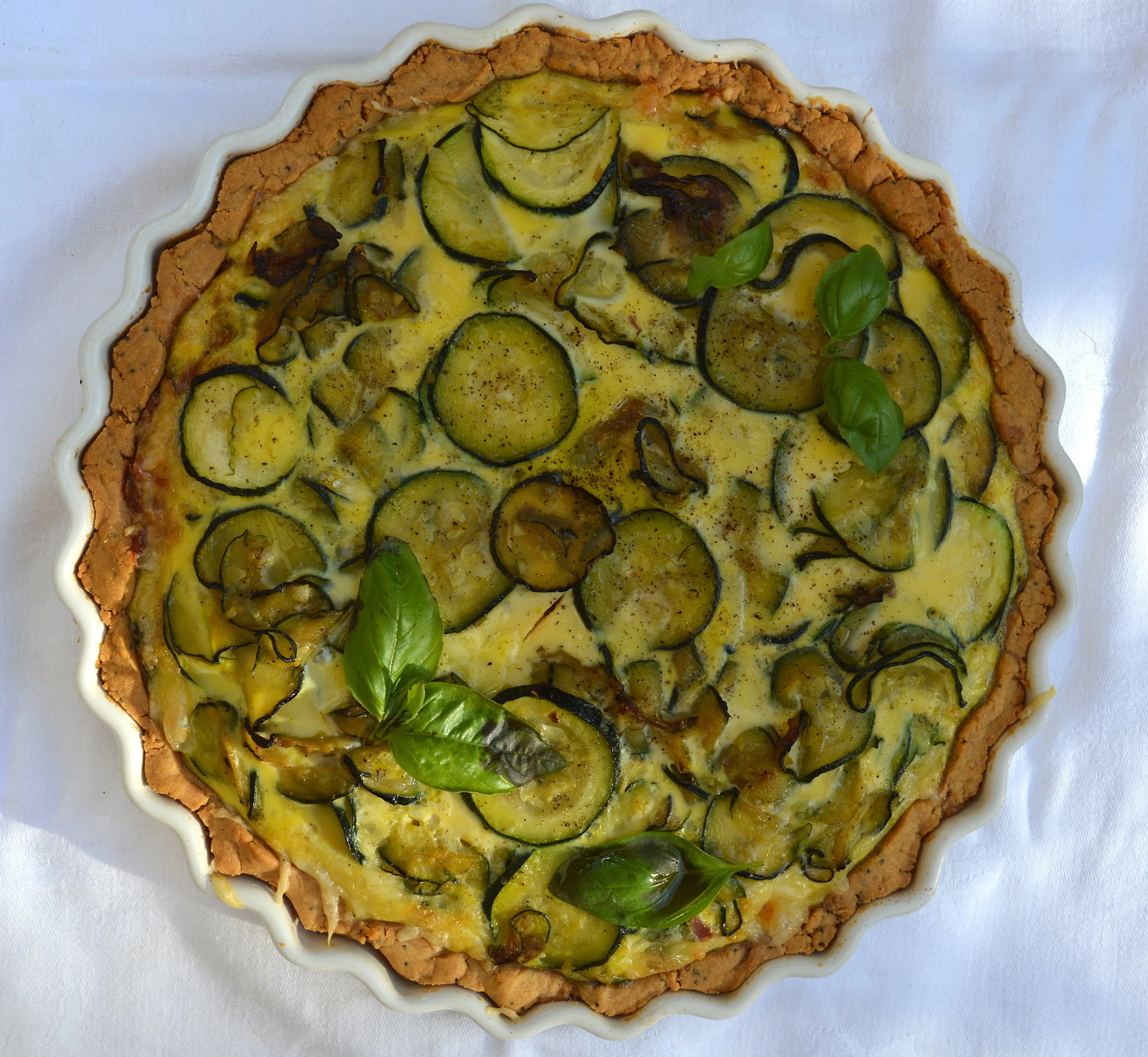 I have been dreaming of the quiche I had at the Chelsea Physic Garden last week and have come up with my own version. I knew that I had to go heavy on the cheese and I've used Comte here but Gruyere would also be delicious. I tried out a new savoury pastry using chickpea flour/gram flour and a little bit of spelt which was more delicate but the eggs tend to seal everything together when the filling goes in. I would use almost all of the pastry to create a good tart base as it's delicate and can crack easily. This was made for dinner one evening here in the south of France and it was gobbled up in seconds. I highly recommend it! Serves 10 Ingredients: For the chickpea pastry 280g chickpea flour/gram flour 50g spelt flour 2 tsp poppyseed 1/2 tsp sea salt 180 cold unsalted butter, cut into cubes 1 medium free-range egg yolk For the filling 4 garlic cloves, diced 2 banana shallots, thinly sliced 2 medium courgettes, thinly sliced 200g smoked lardons 200g Comte cheese, grated 3 tbsp extra virgin olive oil 8 medium free-range eggs, lightly beaten handful fresh basil leaves, roughly torn sea salt and black pepper Begin with the pastry and add both flours, poppyseed, salt and butter into a mixer with the paddle attachment. Set at a medium speed until the mix starts to blend together and become crumbly. This will take about 5 minutes. Then add the egg yolk and it should start to come together into a ball and if not use your hands to blind it. Wrap pastry up in cling film and leave to rest for an hour in the fridge. Lightly butter a 10inch loose-bottom tart dish and use a grater to grate the pastry into the dish. Use your hands to neatly mould it round the tart dish. Do not worry if you have a little left over as your dish maybe not need all of it. Place a sheet of baking parchment over the tart dish and either add in some baking beans or some rice will do. Bake for 20 minutes in a preheated 170 degree oven and then carefully remove the beans and blind bake for another 5-10minutes until the top is lightly golden. While the pastry is cooking you can start on the filling. In a frying pan on a medium to high heat add the lardons and sliced shallots to fry until caramelised and crisp. This will take about 10-15 minutes. Use another large frying pan on a medium to high heat and add the olive oil followed by the sliced courgette to fry and after 5 minutes you can add the diced garlic. Move everything around the pan and season with salt and pepper frying for another 5 minutes until the courgettes are golden. Season the beaten eggs with salt, pepper, torn basil and grated cheese and place into the tart case. Then top with the lardons and shallots mix. Spread everything evenly around the tart and then top with the courgettes trying to arrange them in a nice pattern. Place into the oven for 25-30 minutes until the tart is firm to touch and has risen above the tart base. Remove from oven and leave to cool a little before serving. Tart can be eaten hot or cold and is delicious with a crunchy green salad. Bon! x
