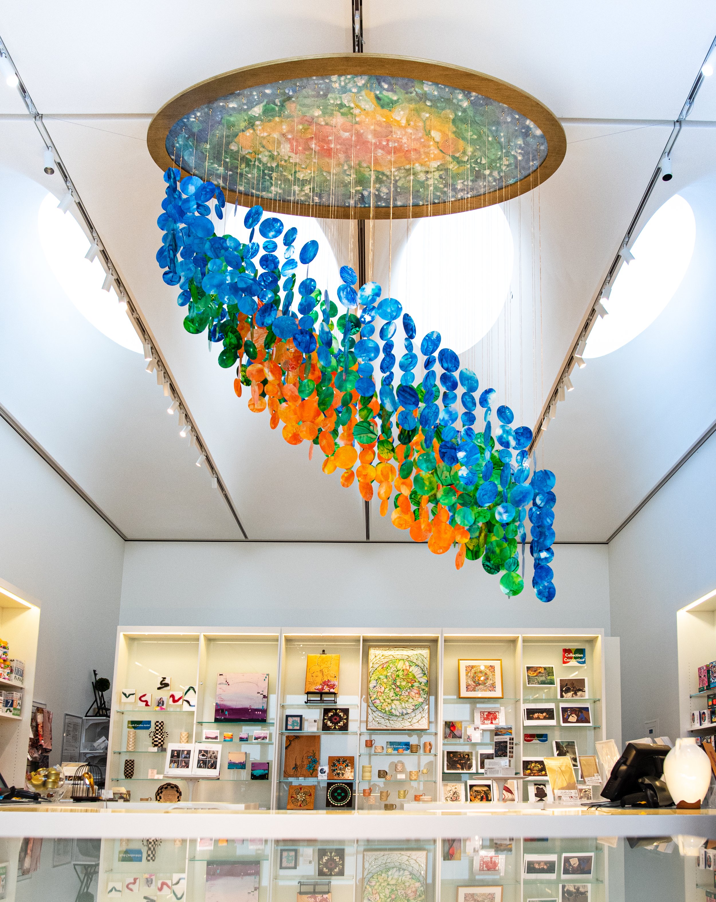   Suspended kinetic installation at North Carolina Museum of Art gift shop, giant immersive mobile art, Raleigh North Carolina installation artist, colorful kinetic blue green orange hanging sculpture, immersive installation, suspended sculpture, Ral