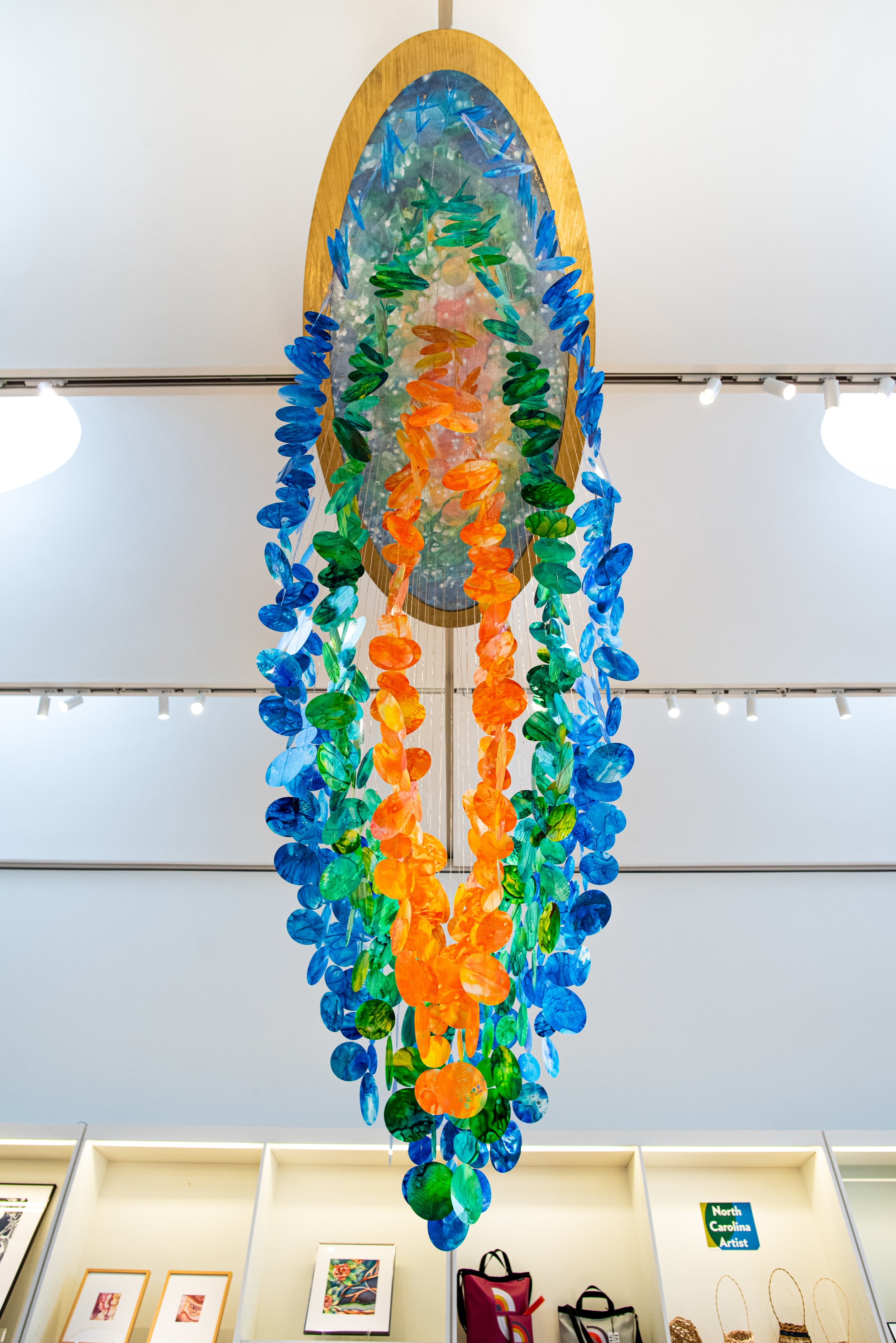   SSuspended kinetic installation at North Carolina Museum of Art gift shop, giant immersive mobile art, Raleigh North Carolina installation artist, colorful kinetic blue green orange hanging sculpture, immersive installation, suspended sculpture, Ra