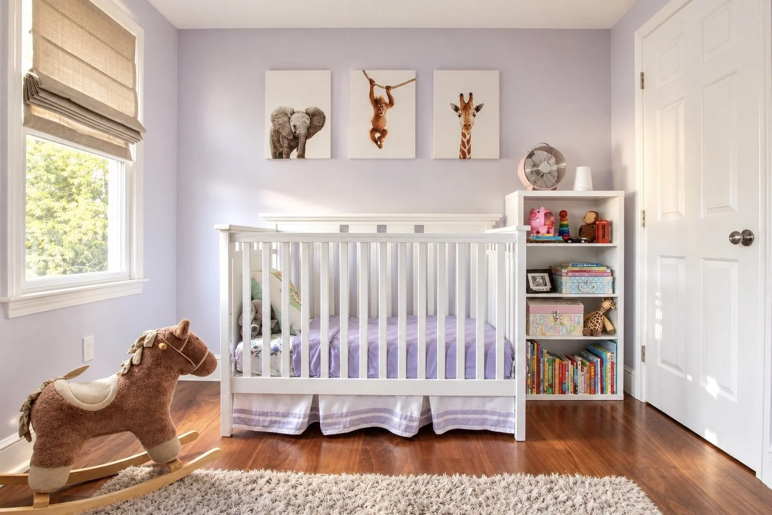 A baby's nursery with a white crib, a rocking horse, a white bookshelf filled with toys and books, and animal artwork on the wall.