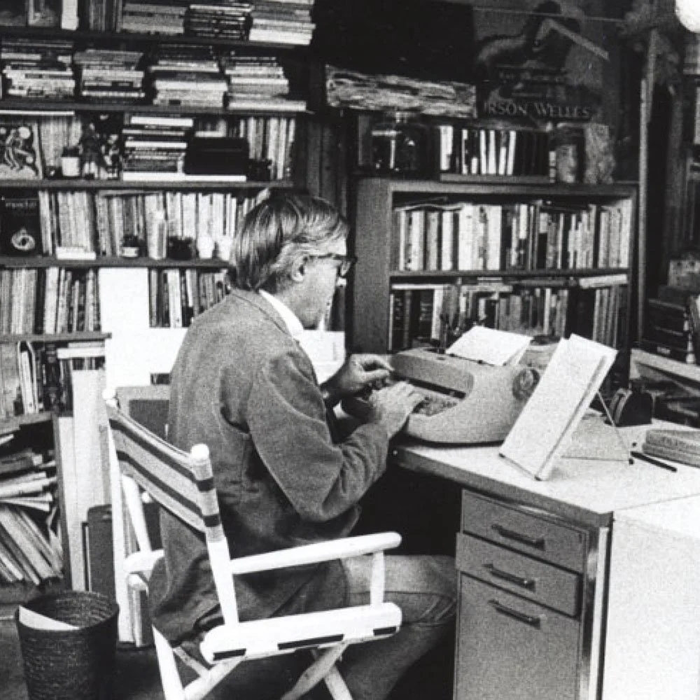 The image shows American author Ray Bradbury typing at his desk in his book-filled home office.