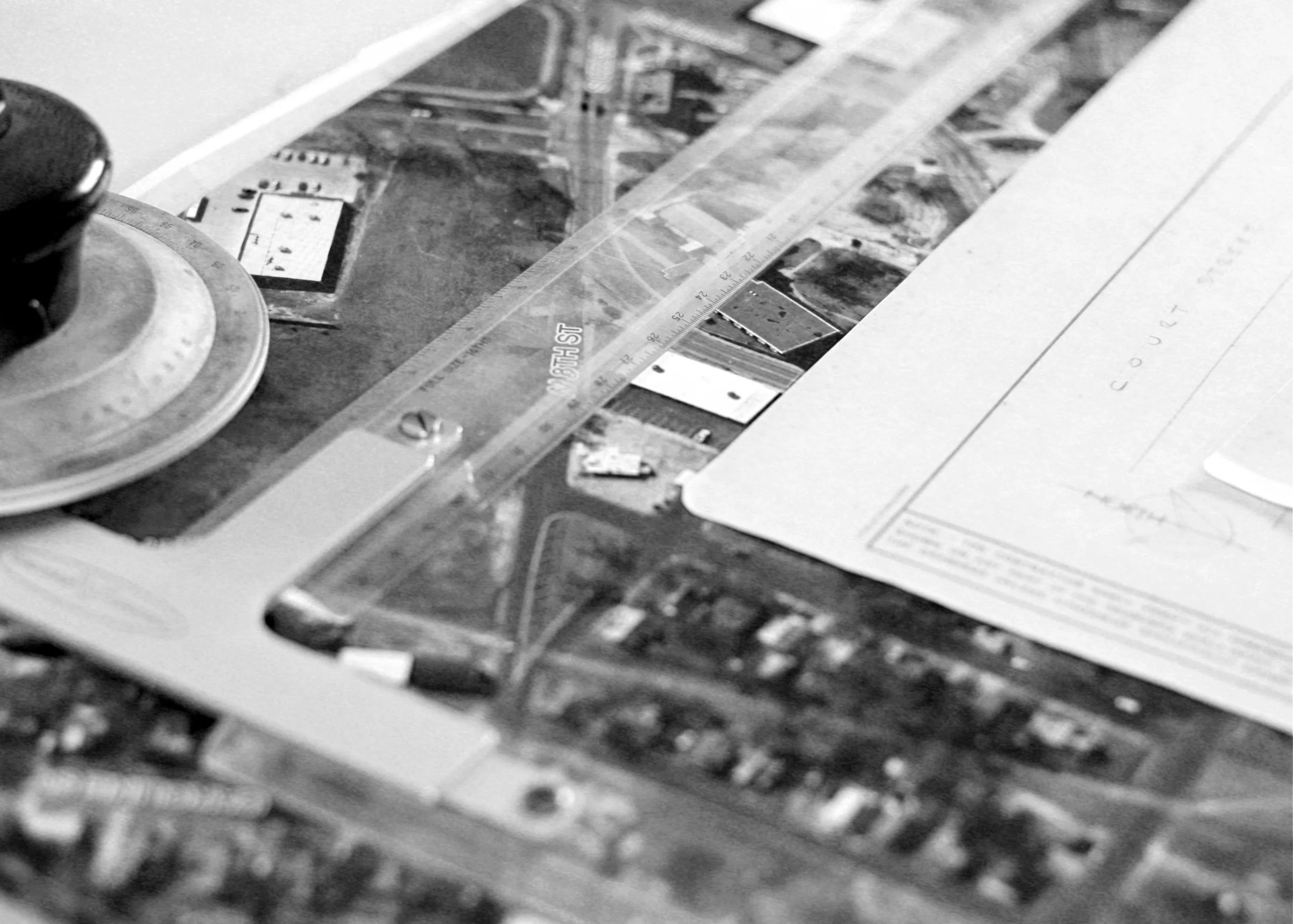 Close-up of a map or diagram with a transparent ruler, a paper with handwritten notes, and an object that appears to be a stanchion or a similar device on a desk.