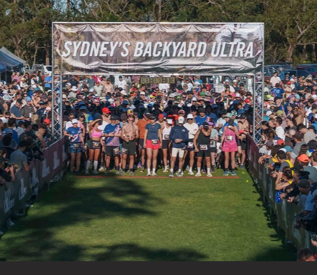 Start line at Sydney's Backyard Ultra race with a large crowd of runners and spectators under a banner.