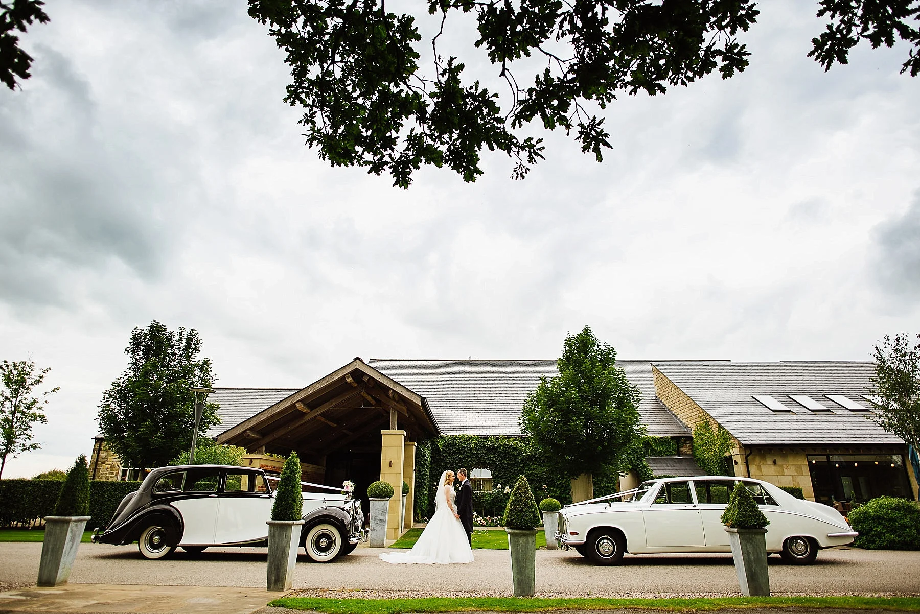 Wedding portrait of the Bride and Groom with their two cars outside Stanley House