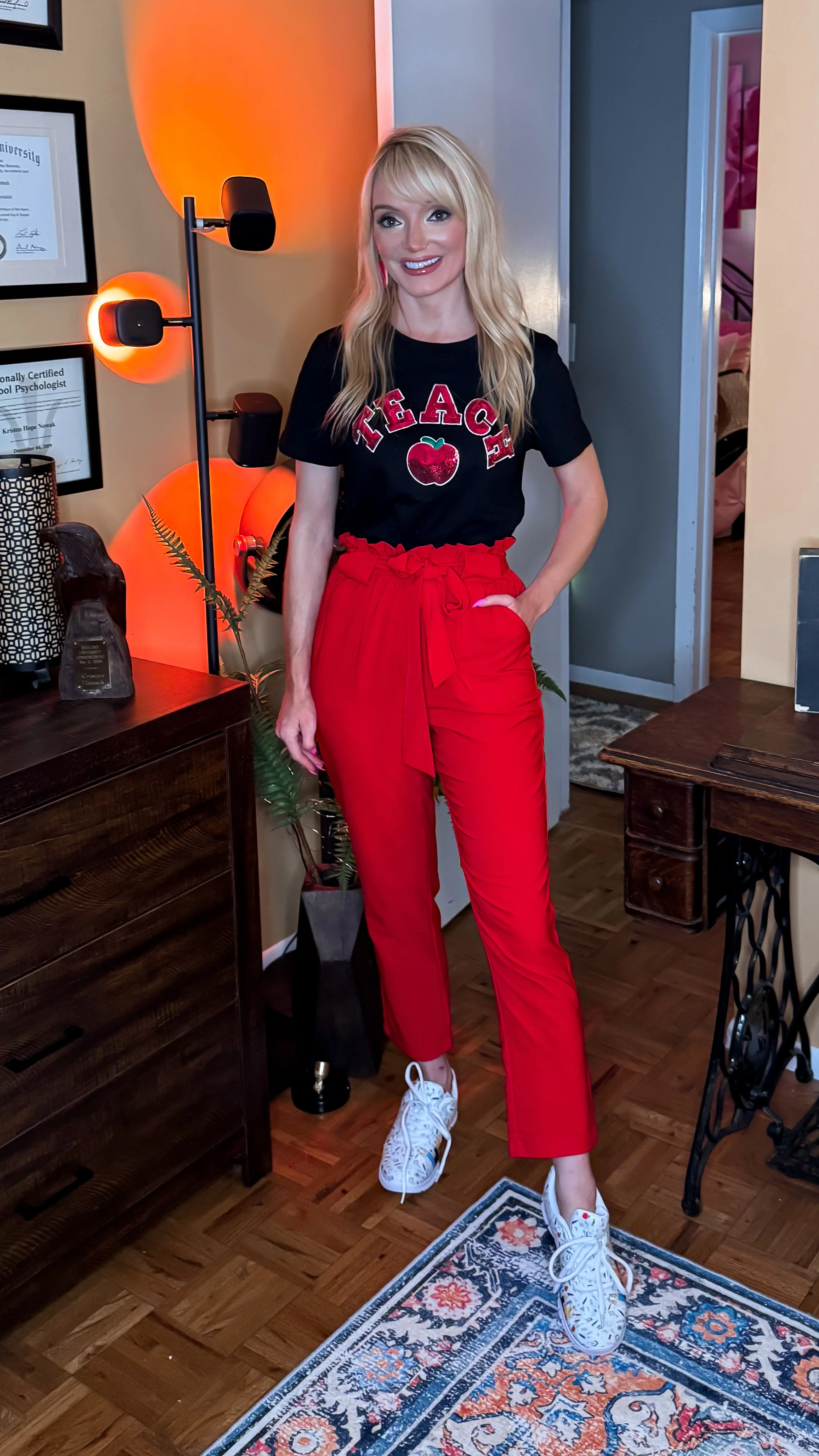  Blonde woman wearing a back to school teacher outfit with a sequin teach tshirt, red paperbag pants, and pencil style sneakers 