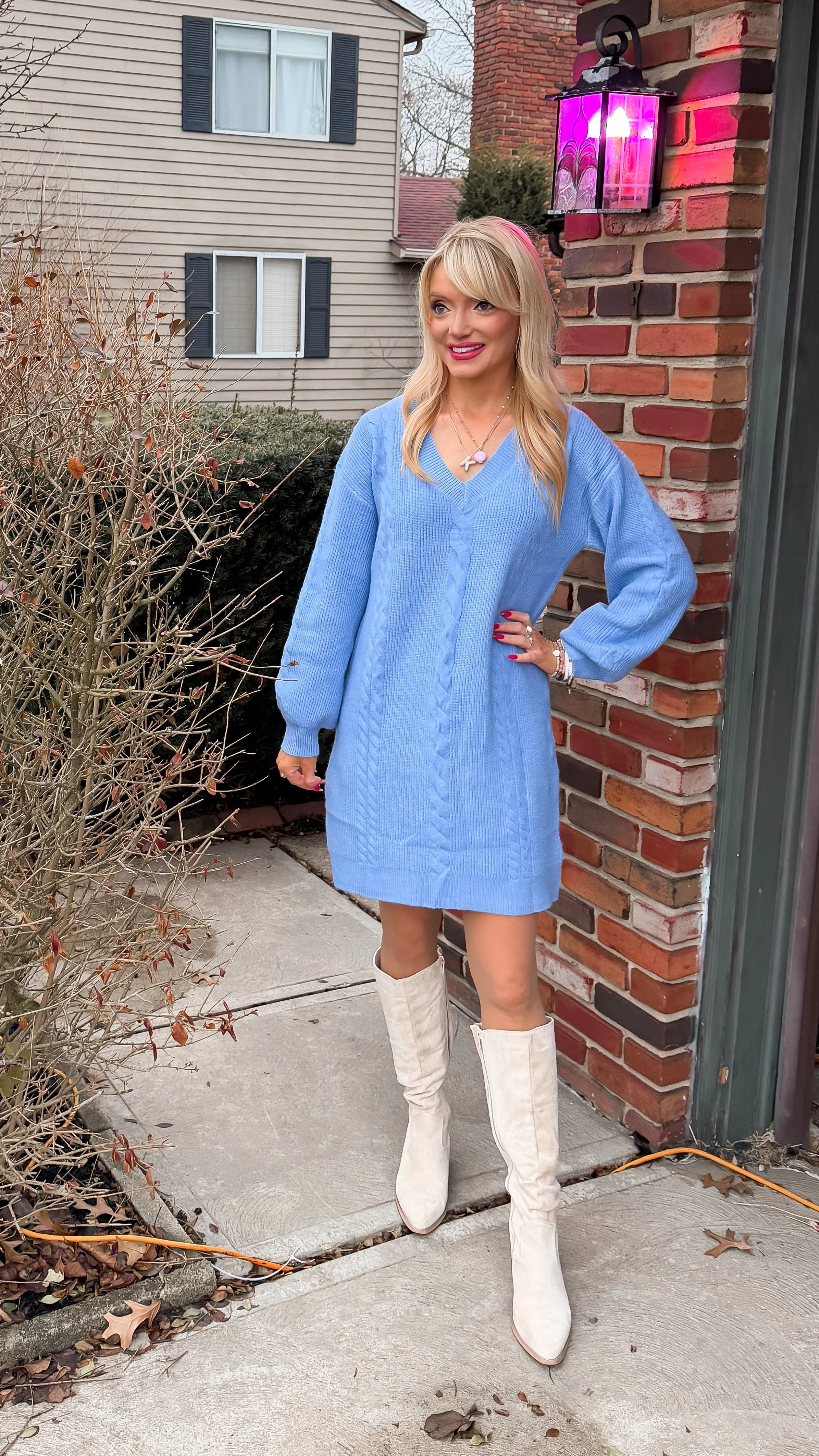 Woman with long blonde hair wear slouchy v neck light blue sweater dress with knee high sand colored suede boots all from Amazon