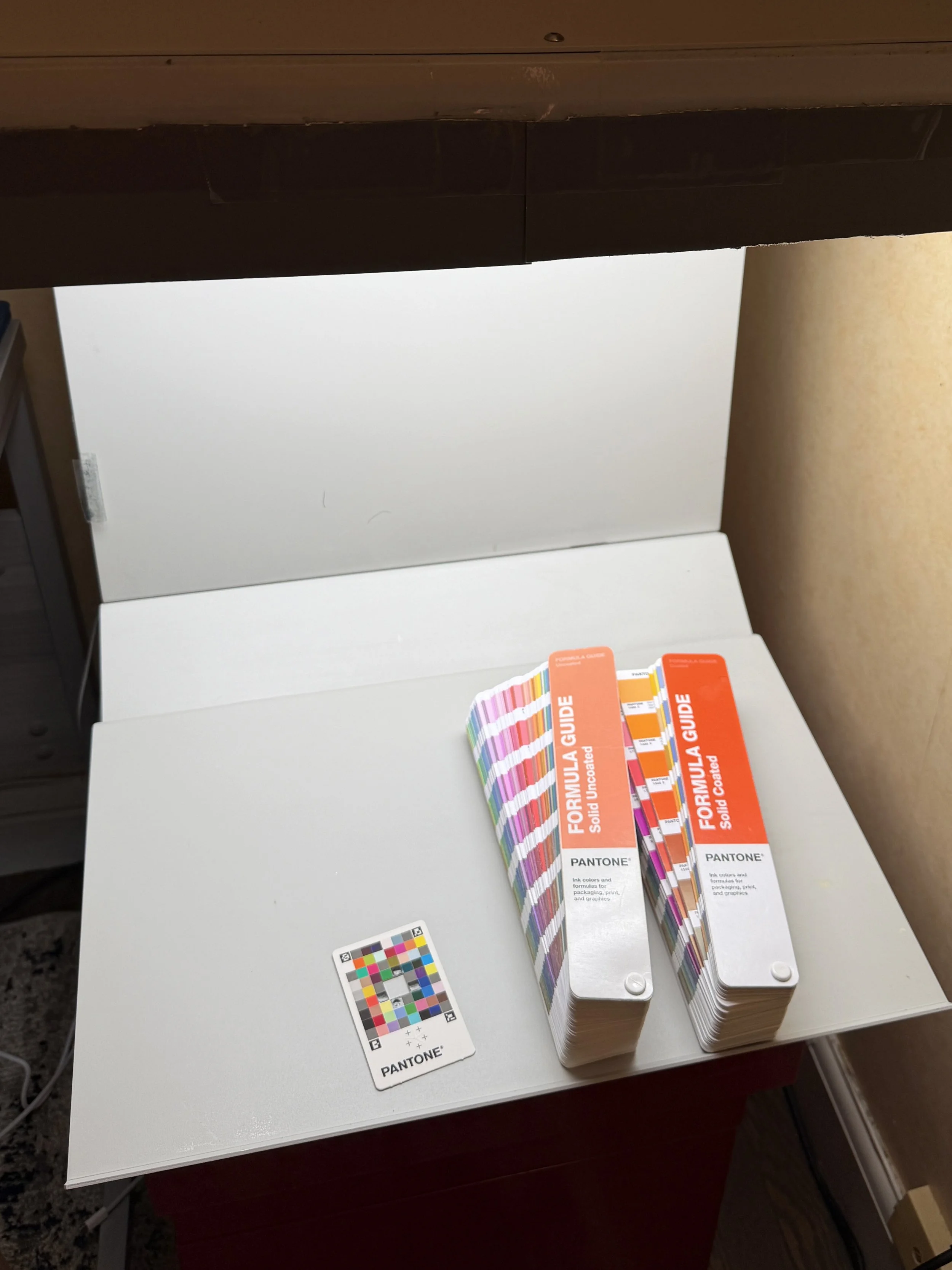 Pantone Formula Guides, Pantone Color Match Card, and GTI PDV viewing booth used for calibrated color evaluation during catalog production.