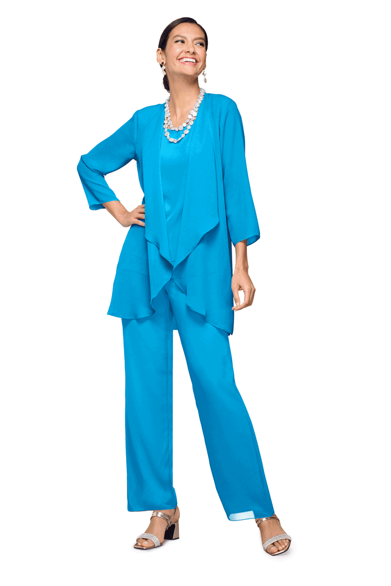 A woman in a bright blue pantsuit and matching top, accessorized with pearl jewelry, standing confidently with one hand on her hip and smiling.