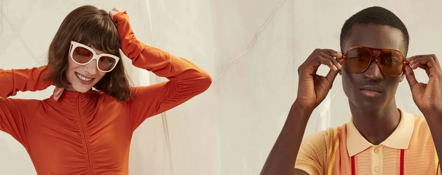 Two women wearing sunglasses, one with a bright orange shirt and the other with a light orange polo, smiling and posing for the photo.