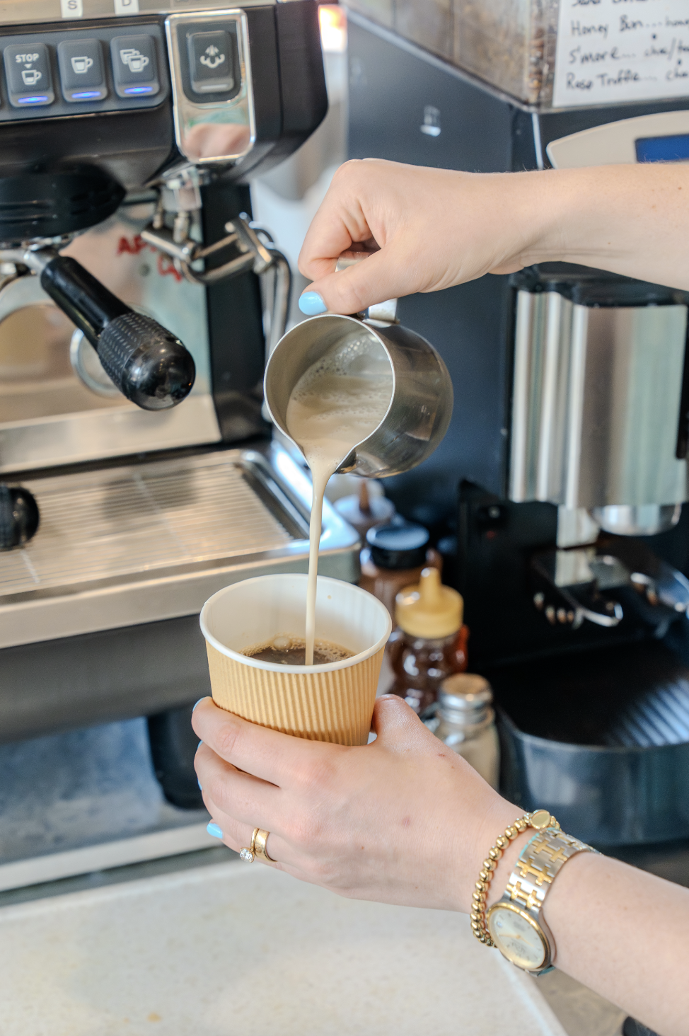 A barista is pouring steamed milk into a cup of coffee.
