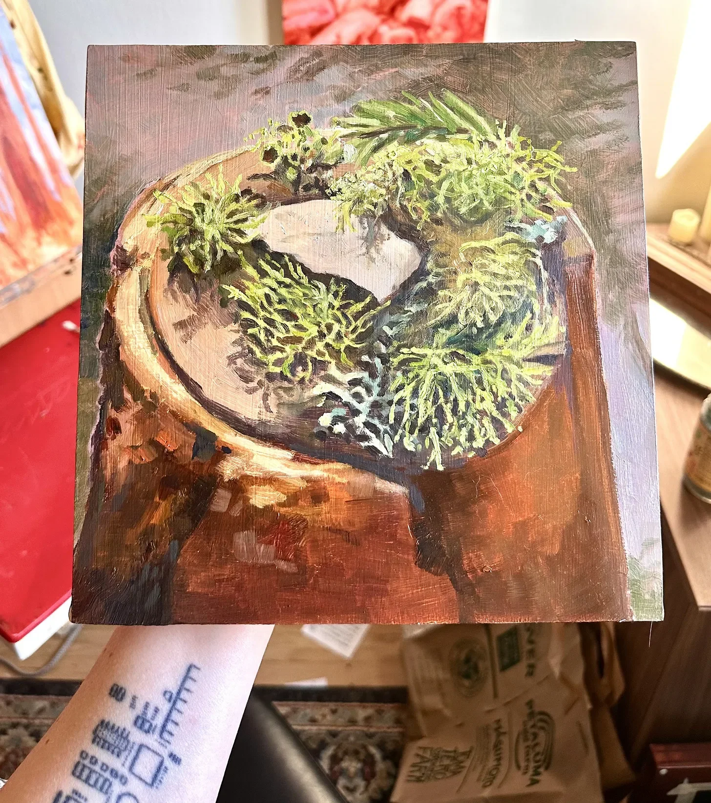 image of a person holding an oil painting, in progress, of the Lichen altar I made while camping in Sequoia National Forest.