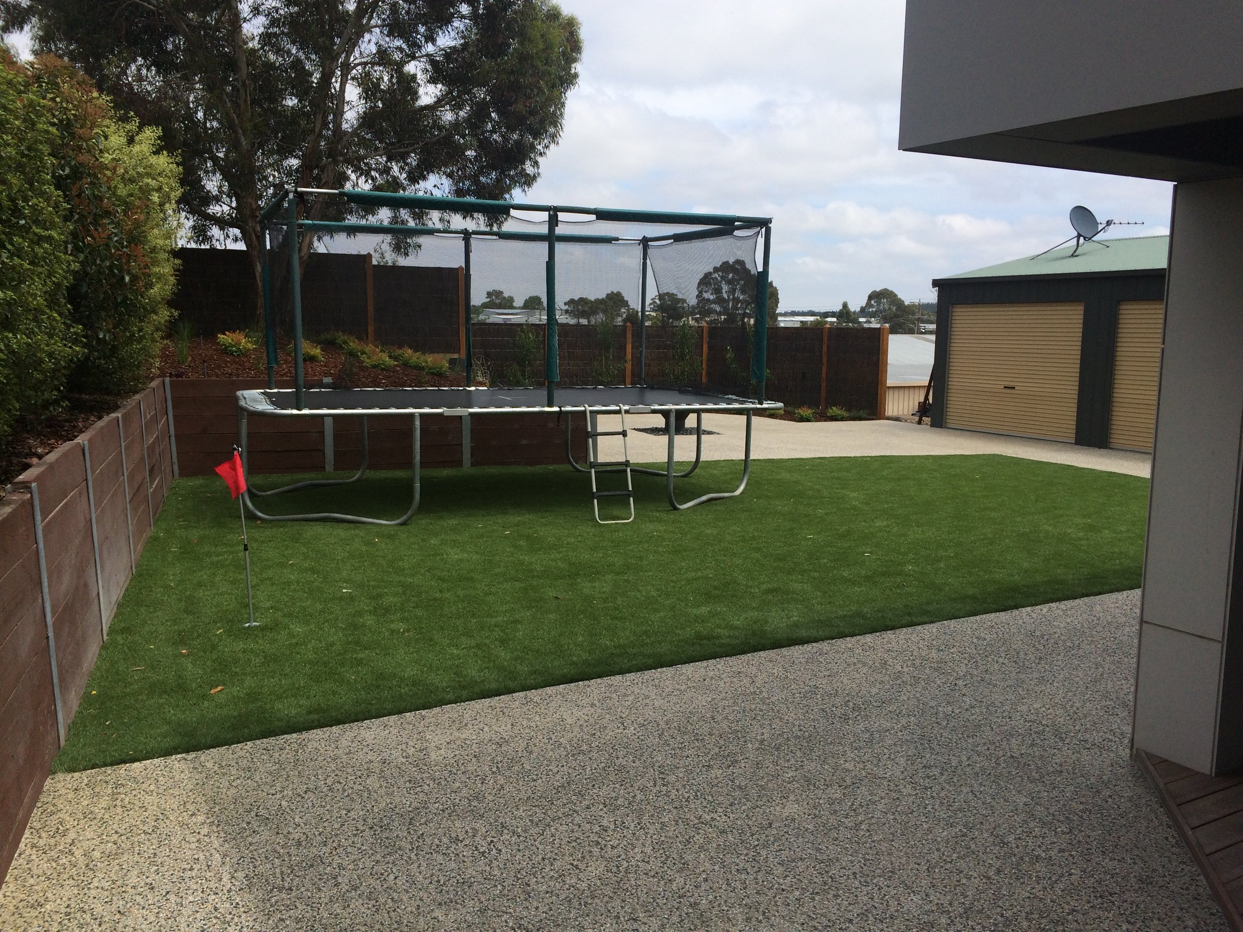 Synthetic turf, retaining wall with garden bed, exposed aggregate, fire pit and golf hole