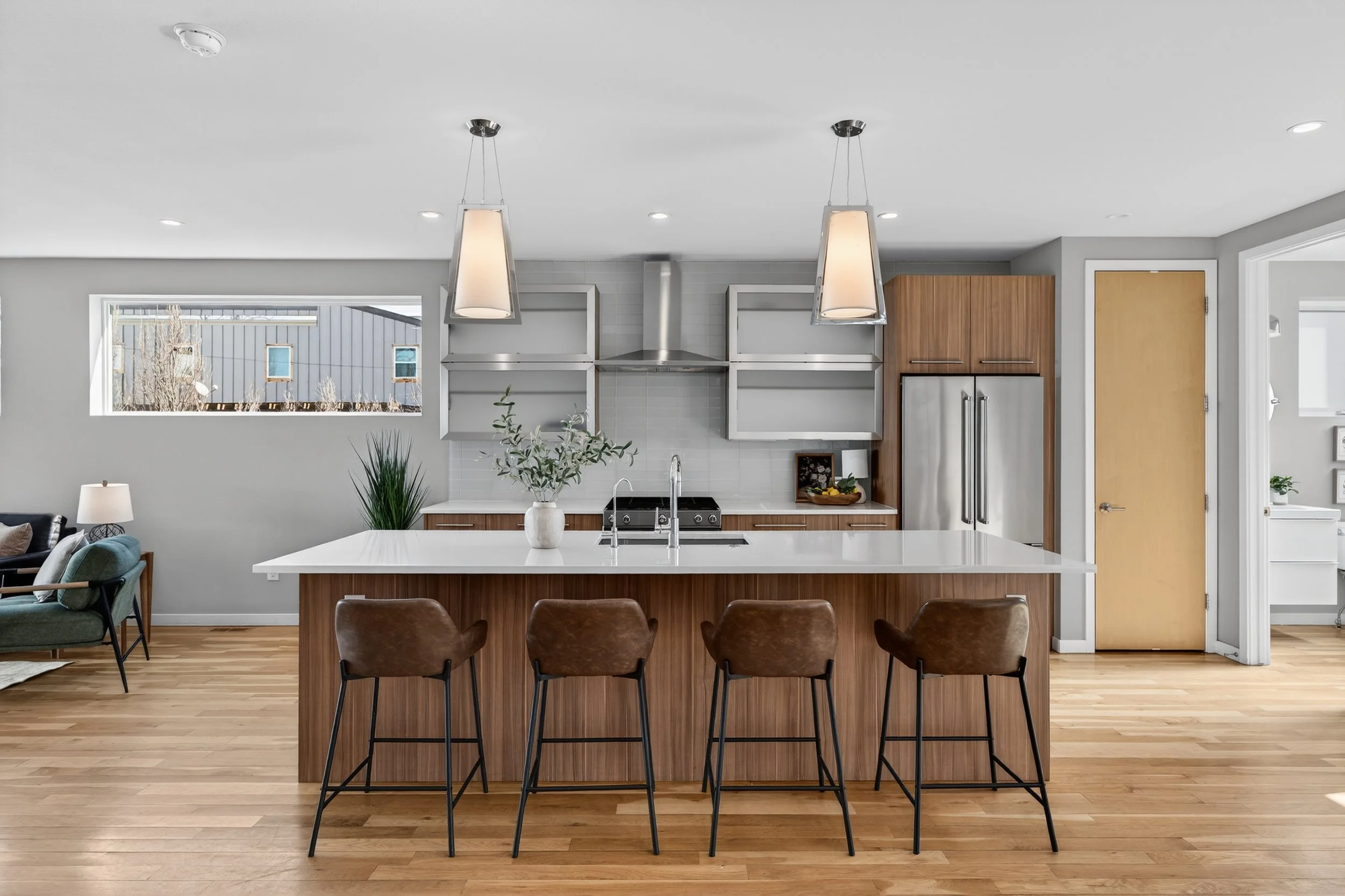Modern kitchen with a white island, brown leather bar stools, stainless steel appliances, open shelving, and hardwood floors.