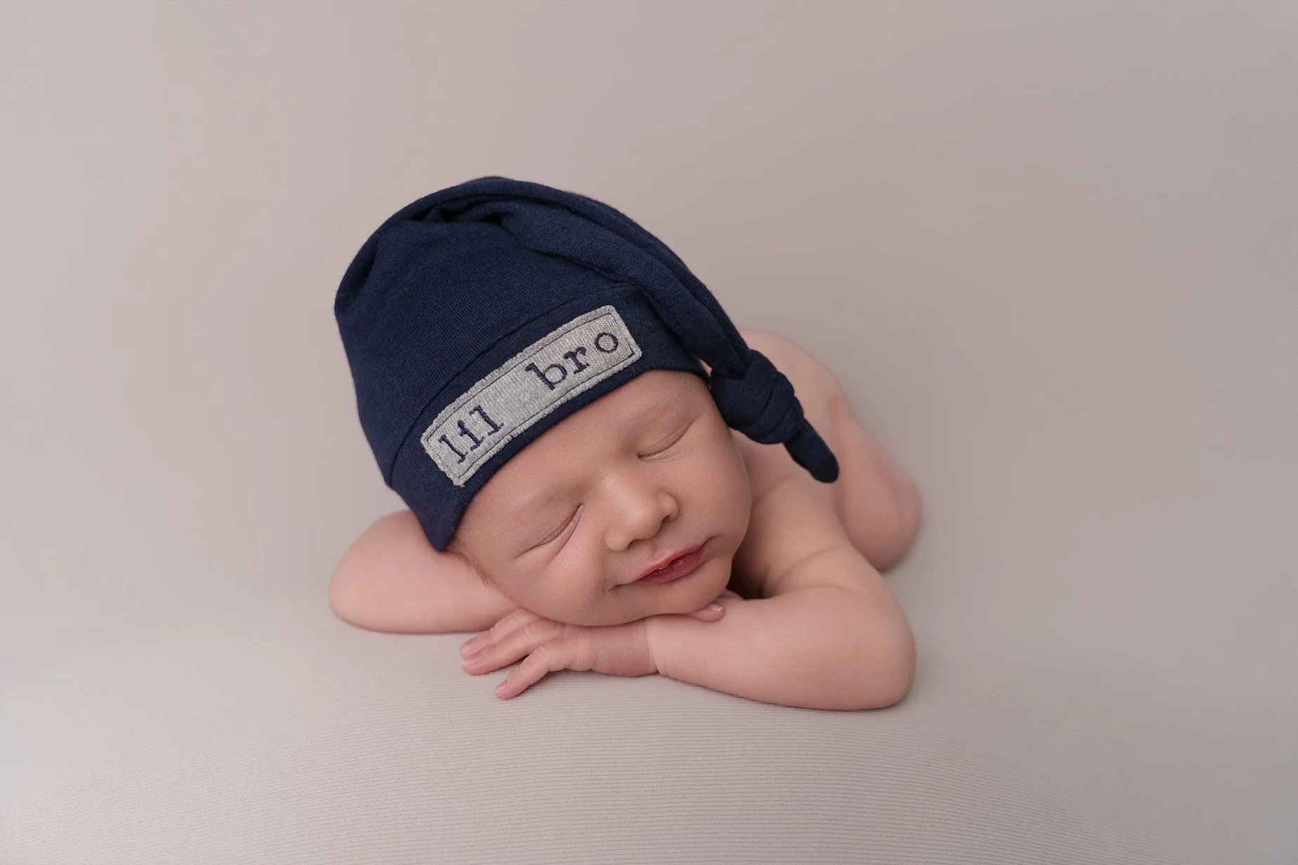 Sleeping newborn baby boy wearing a navy hat on a neutral backdrop during a newborn photography session near Edwardsville, IL.