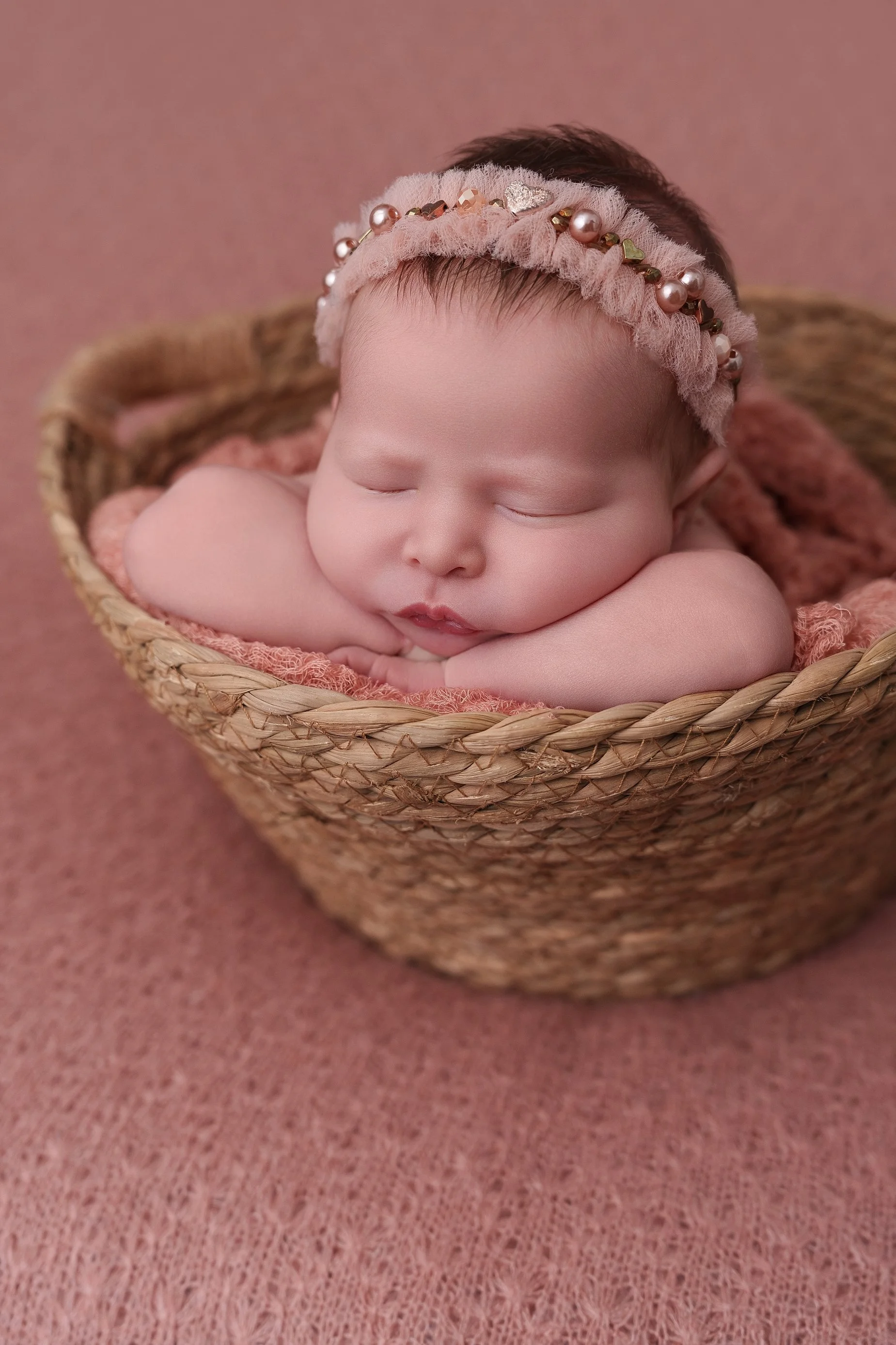Baby girl posed in a woven basket with dusty pink backdrop by Edwardsville IL newborn photographer Conner James Photography