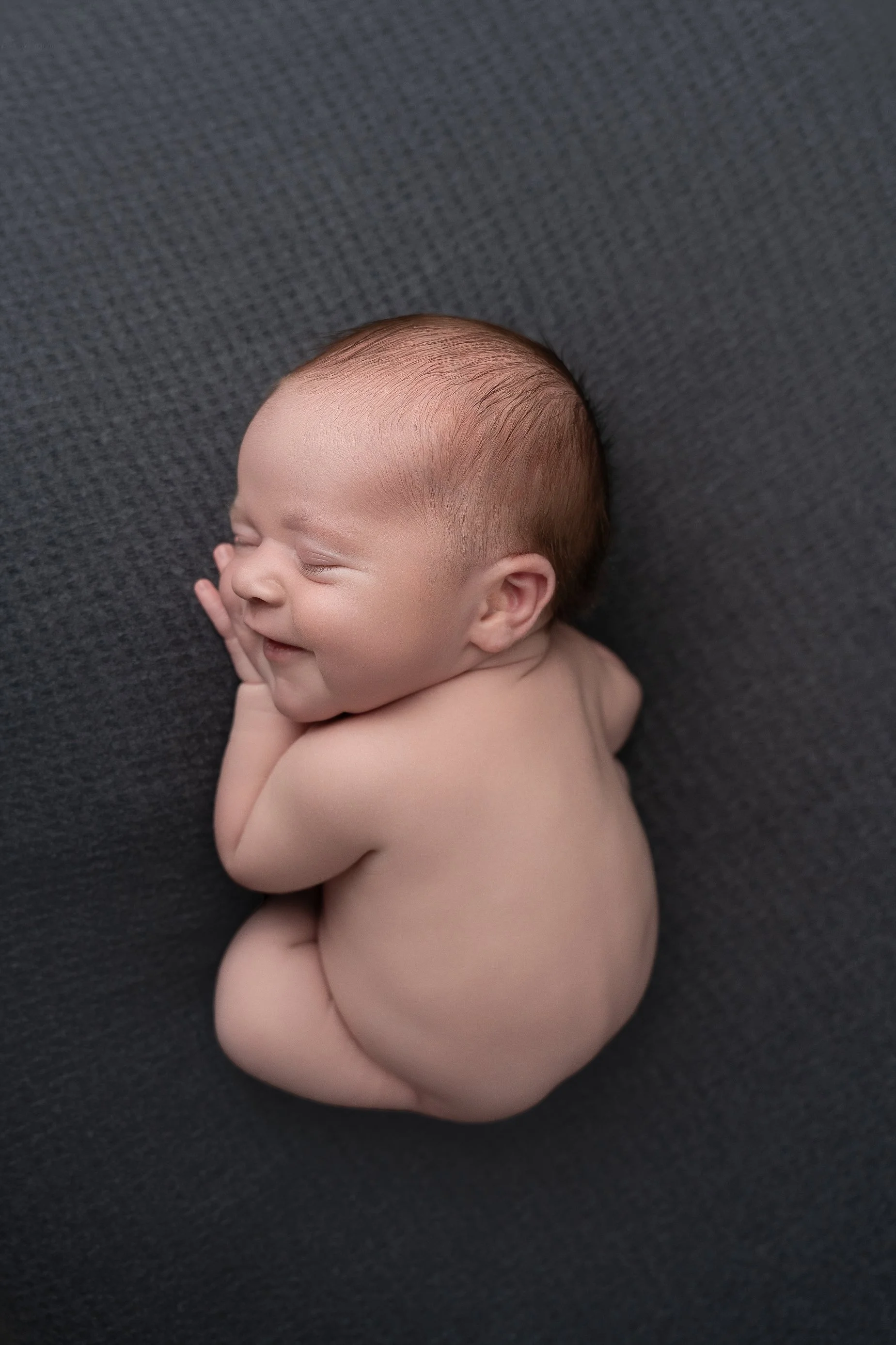 Sleeping newborn baby boy posed on dark blue textured fabric during a professional newborn photography session in Edwardsville Illinois.