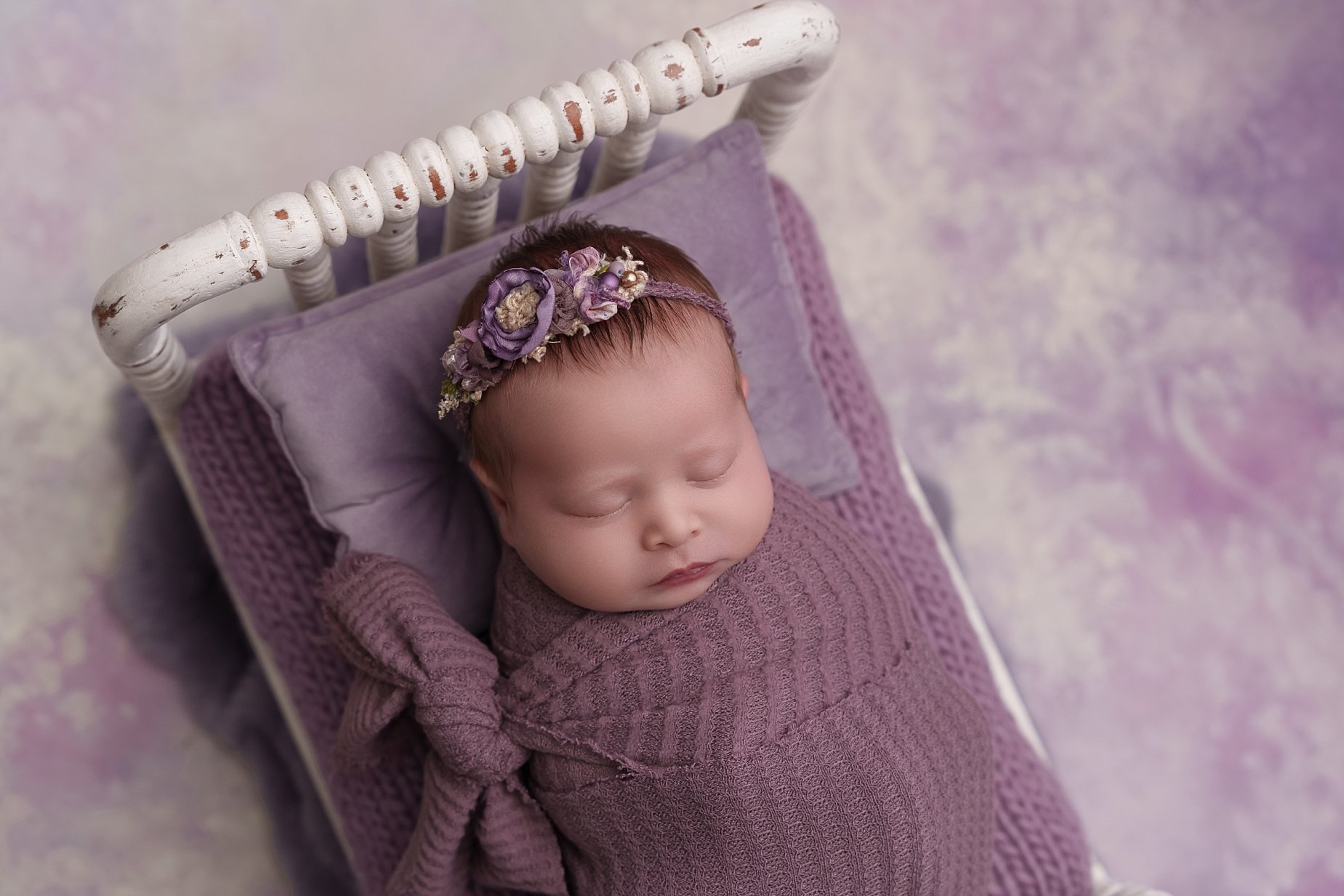 Newborn baby girl wrapped in purple on vintage bed by Edwardsville and Glen Carbon newborn photographer