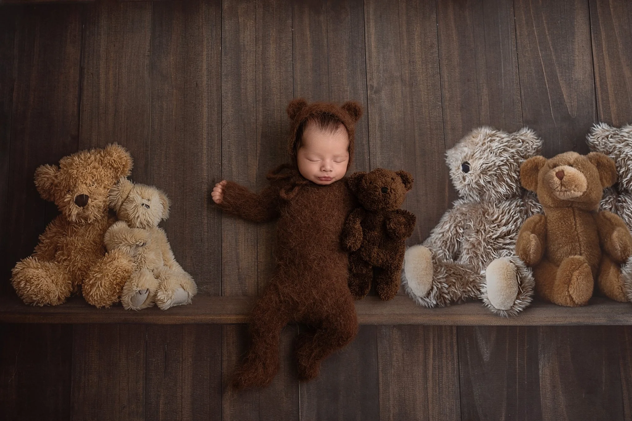 Newborn in fuzzy brown bear outfit lying with teddy bears during studio session near Collinsville, Troy, and Maryville IL.