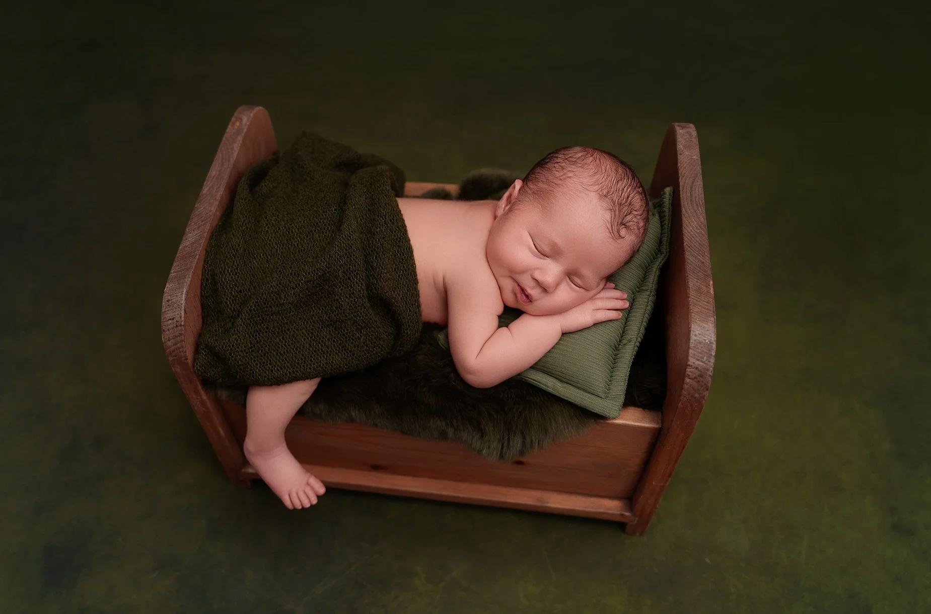 Sleeping newborn baby posed safely on a green pillow in a wooden bed at a Glen Carbon newborn photography studio serving Edwardsville, IL.
