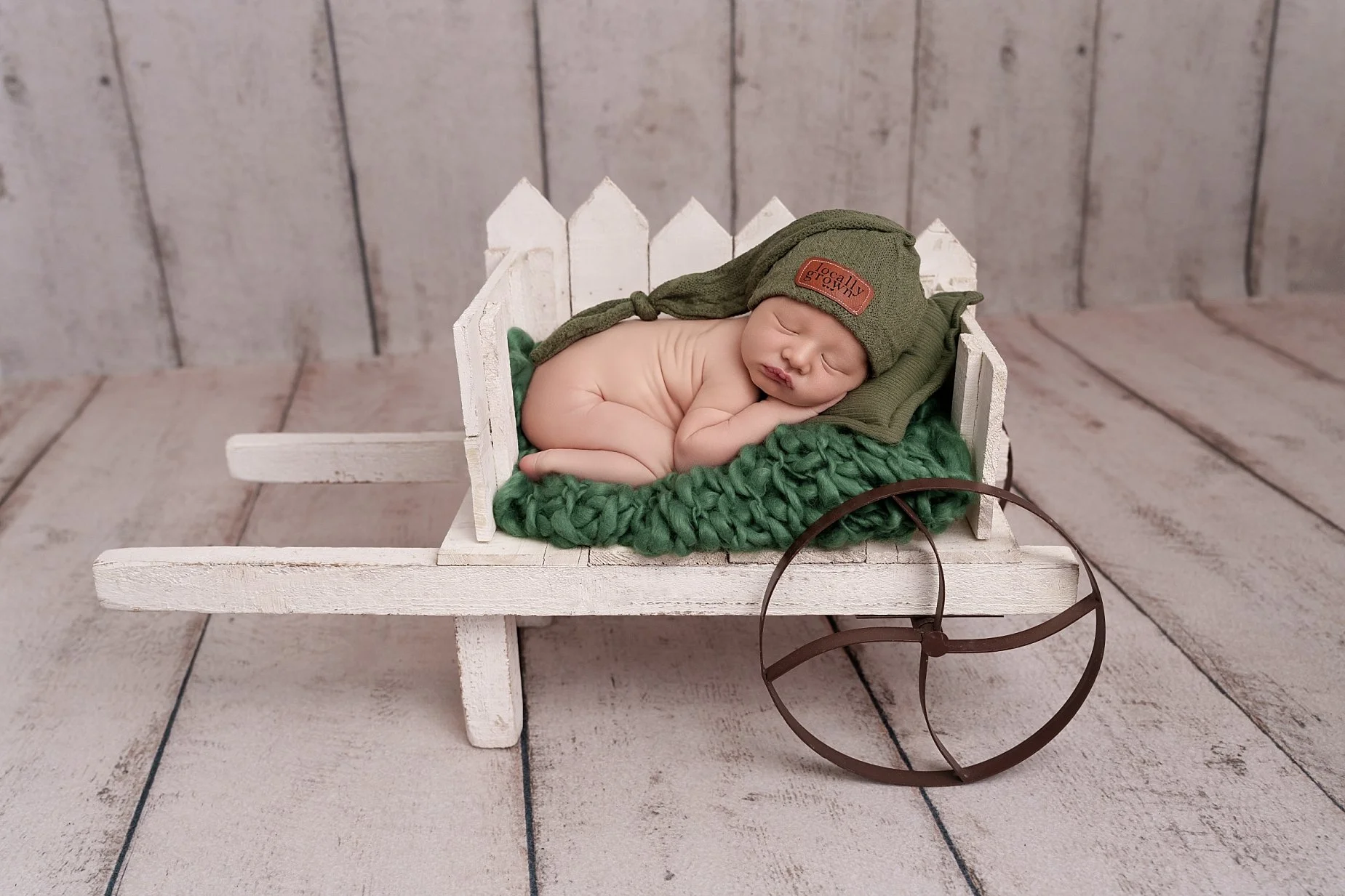 Baby boy sleeping in a rustic white wagon with green newborn accessories photographed by an Edwardsville newborn photographer in Glen Carbon, IL.