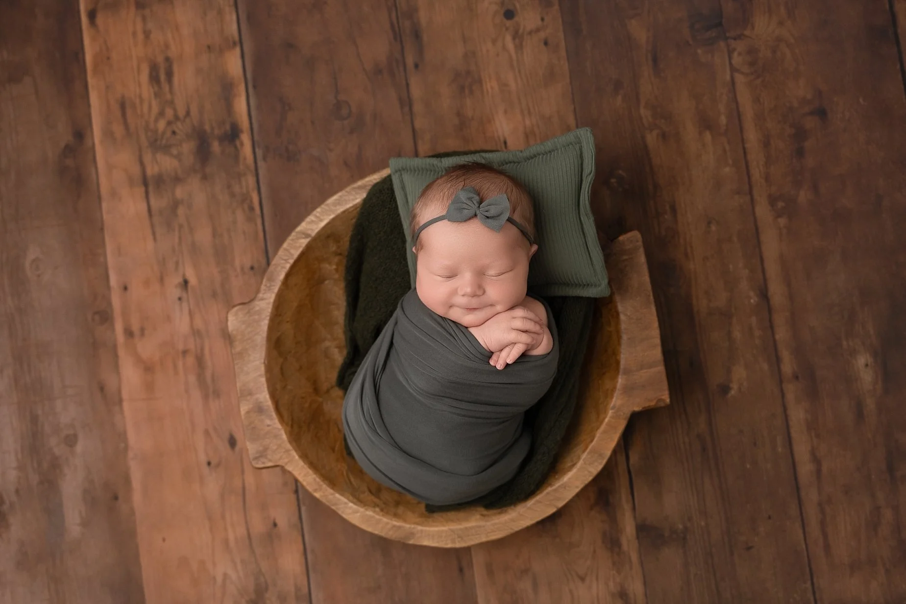 Sleeping newborn baby girl wrapped in sage green fabric in a wooden bowl by Edwardsville newborn photographer.