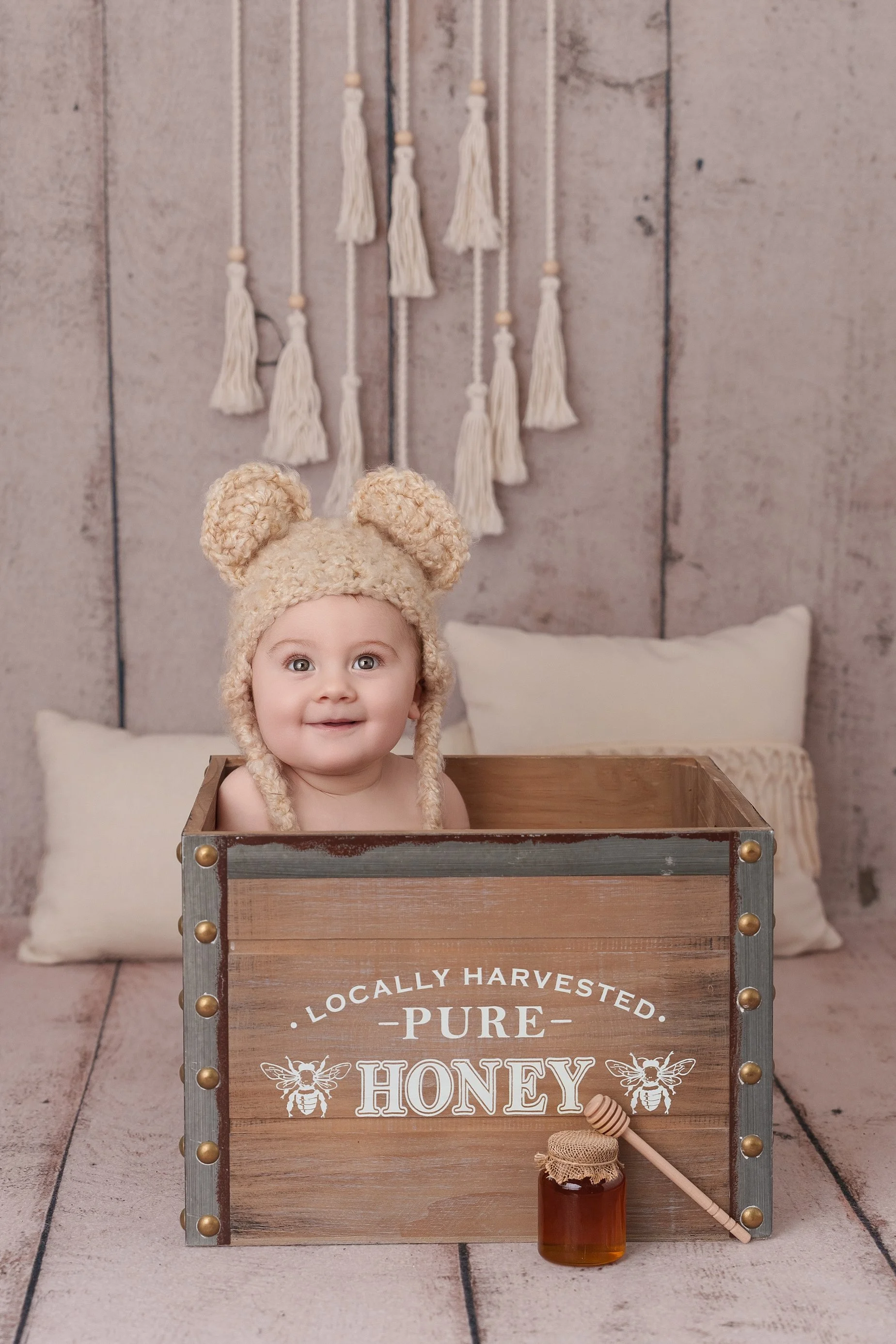 Adorable 9-month-old baby wearing a teddy bear hat sitting inside a honey crate during a milestone photography session in Glen Carbon, Illinois.