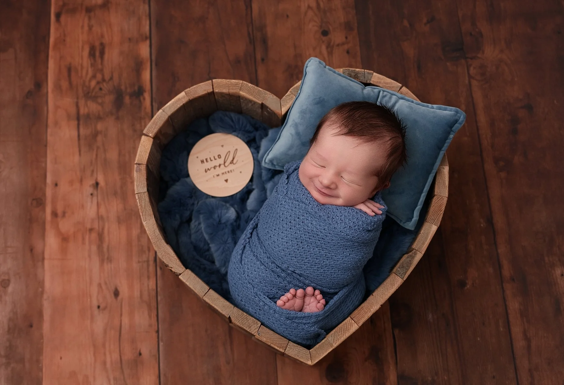 Newborn baby boy wrapped in blue and posed in a wooden heart prop at Conner James Photography, a newborn photography studio near Edwardsville, IL.
