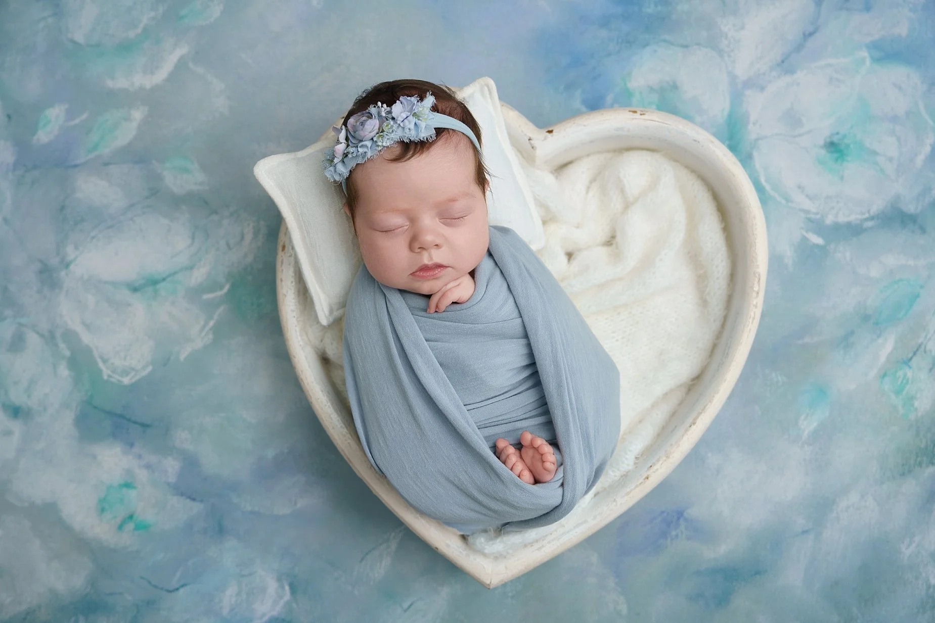 Sleeping newborn baby girl wrapped in soft blue fabric posed in a heart-shaped bowl in a Glen Carbon IL studio.