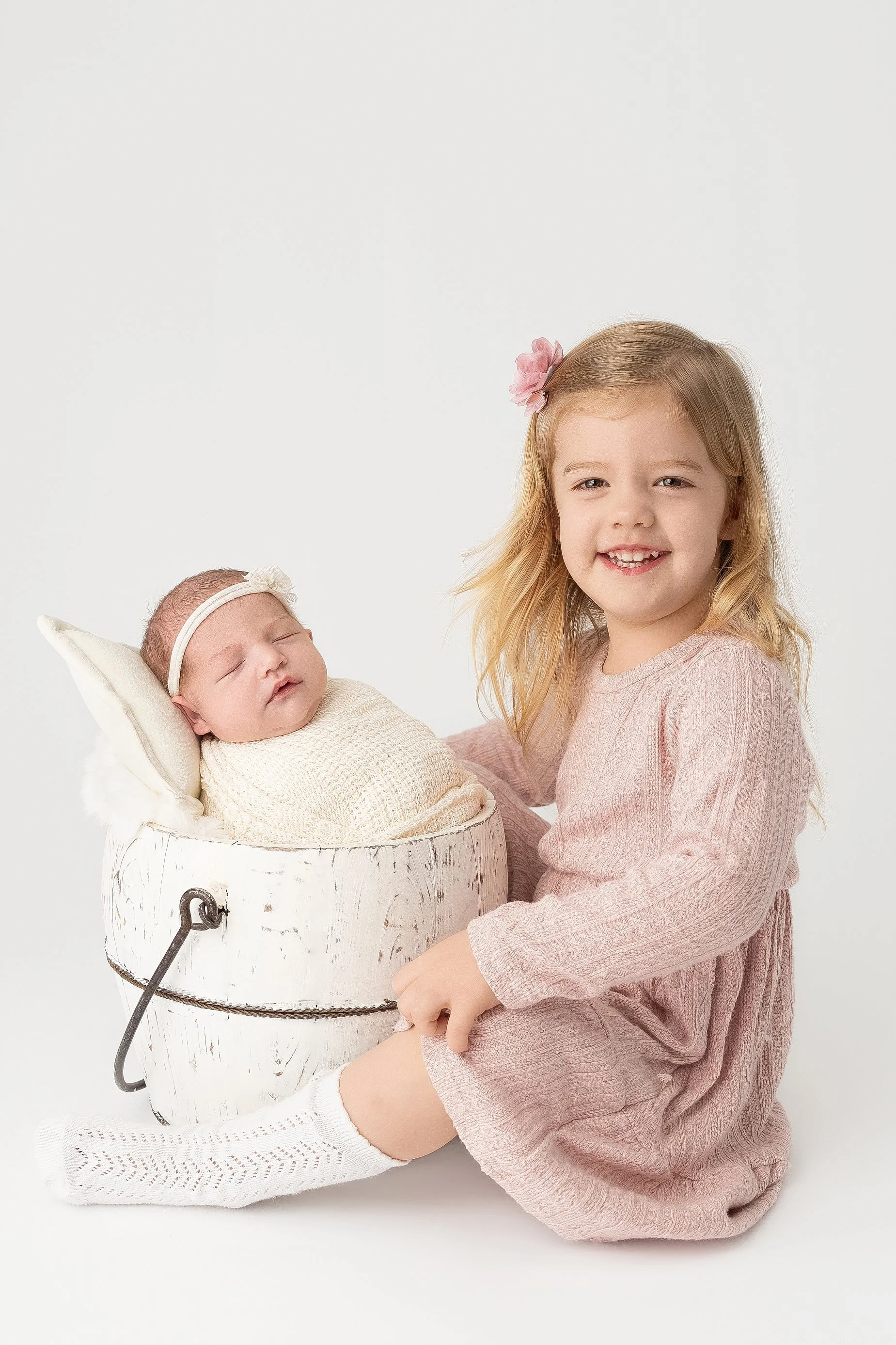 Big sister smiling beside her newborn sibling during a timeless studio newborn portrait session in Edwardsville Illinois.