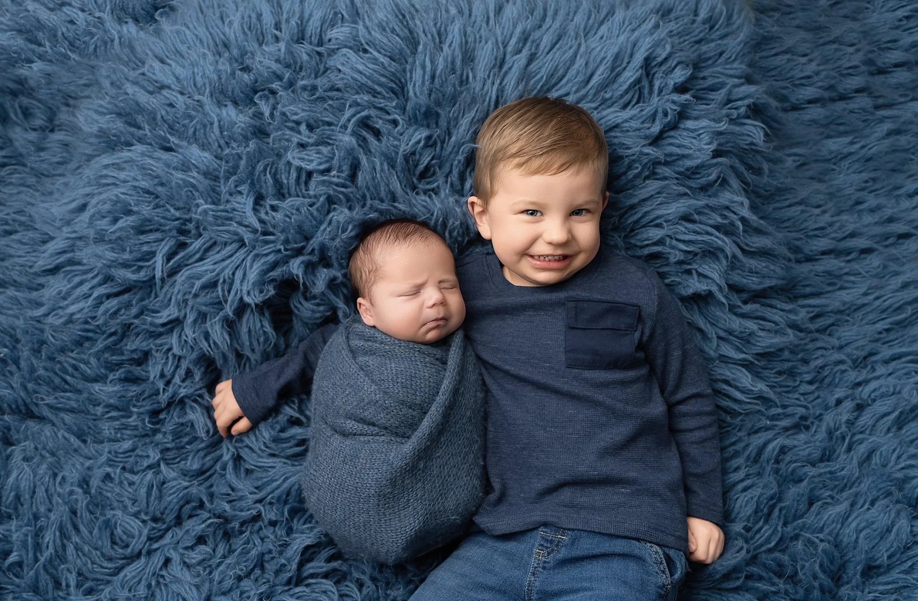 Sibling newborn photo with big brother holding baby on blue textured blanket in Glen Carbon IL studio.
