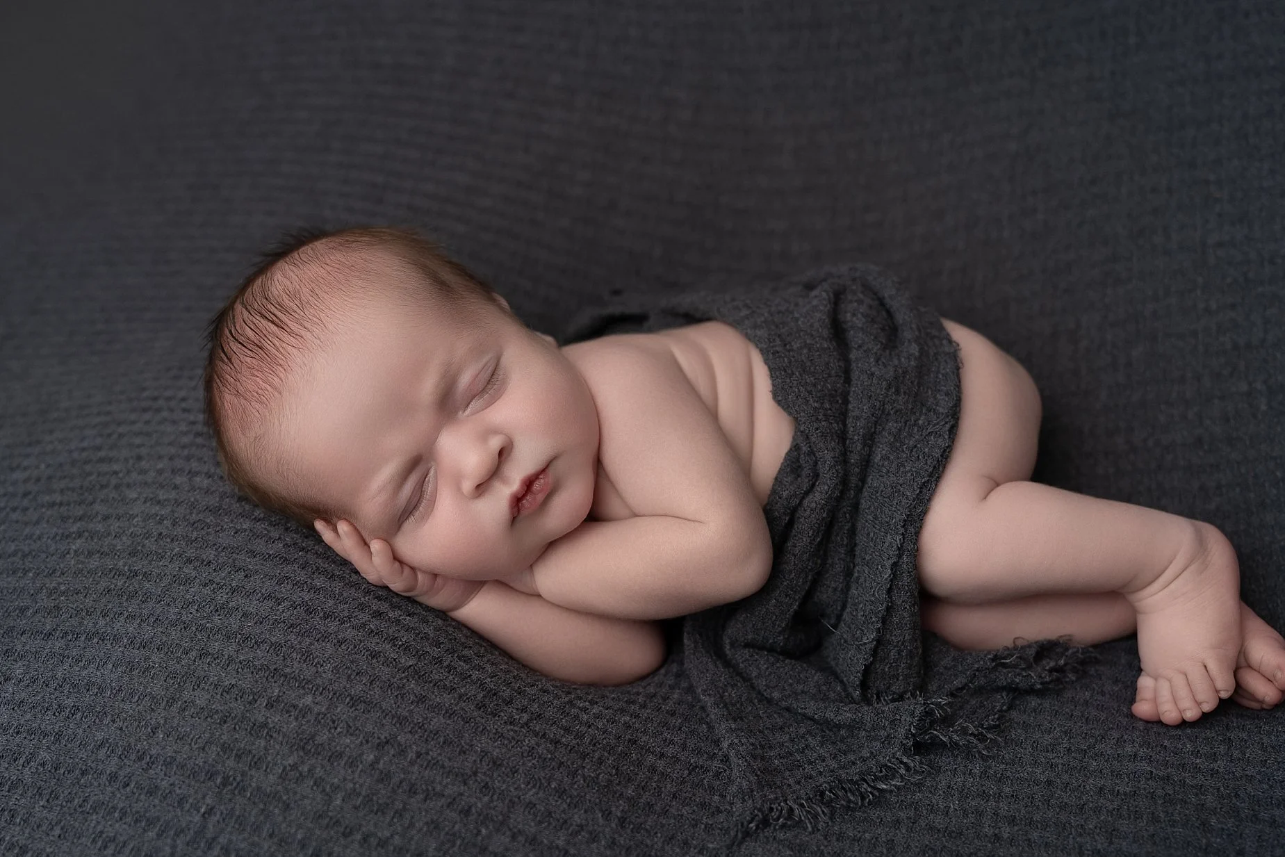 Peacefully sleeping baby boy posed on dark textured fabric during a fine art newborn photography session in Glen Carbon IL.