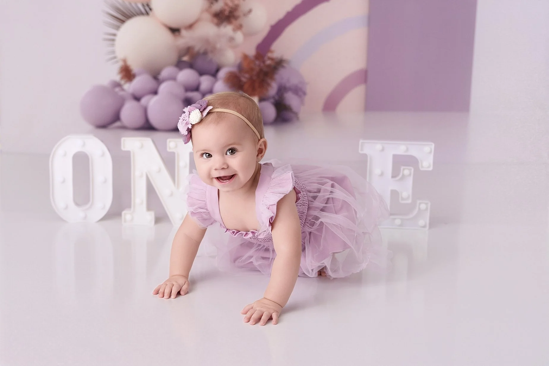 Baby girl crawling in a lavender dress during her first birthday milestone photography session at Conner James Photography near Edwardsville, IL.