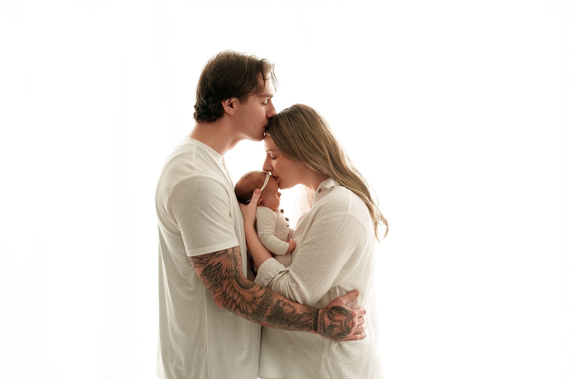 Mom and dad lovingly kiss their newborn baby girl during a family newborn photography session at Conner James Photography in Glen Carbon, Illinois, near Edwardsville.
