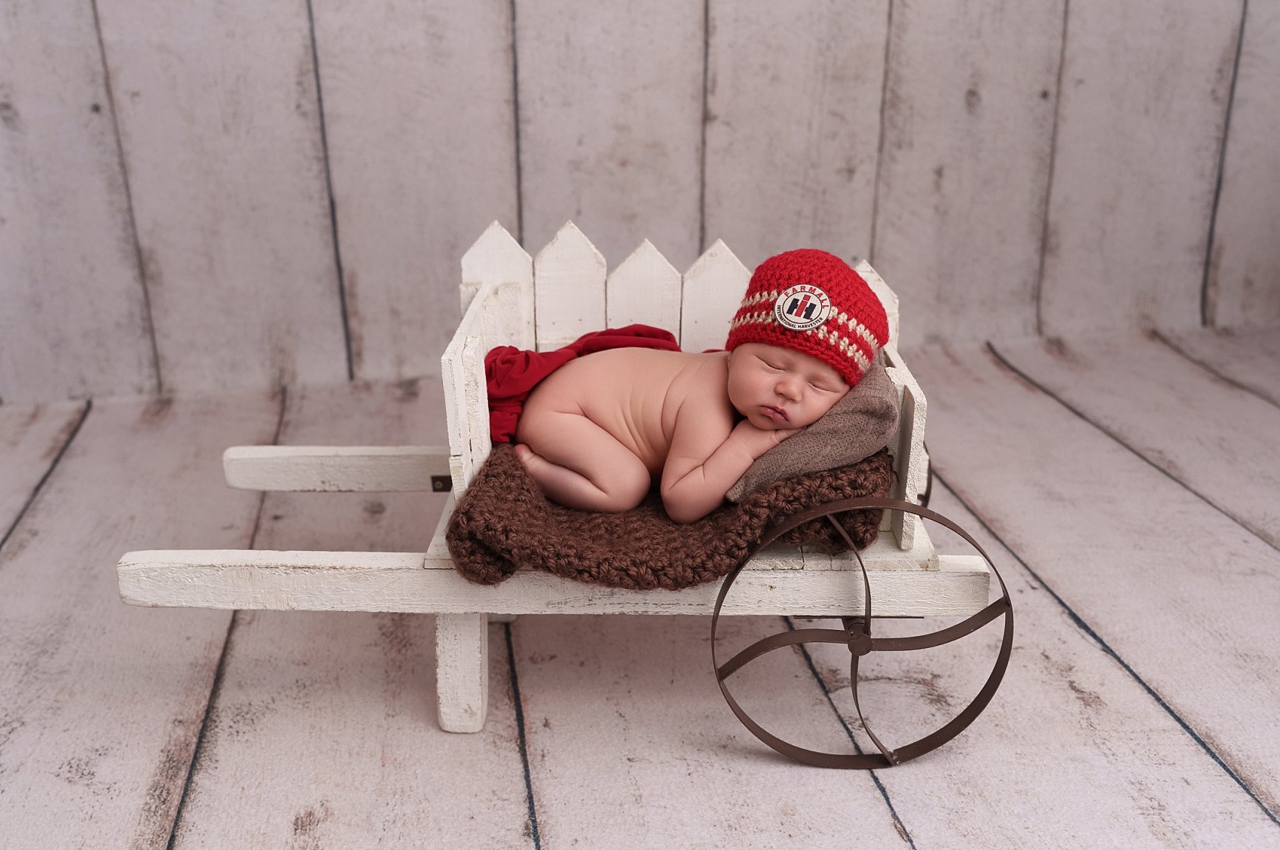 Sleeping newborn baby posed in a rustic white wagon with a red knit hat during a newborn photography session near Edwardsville, Illinois..