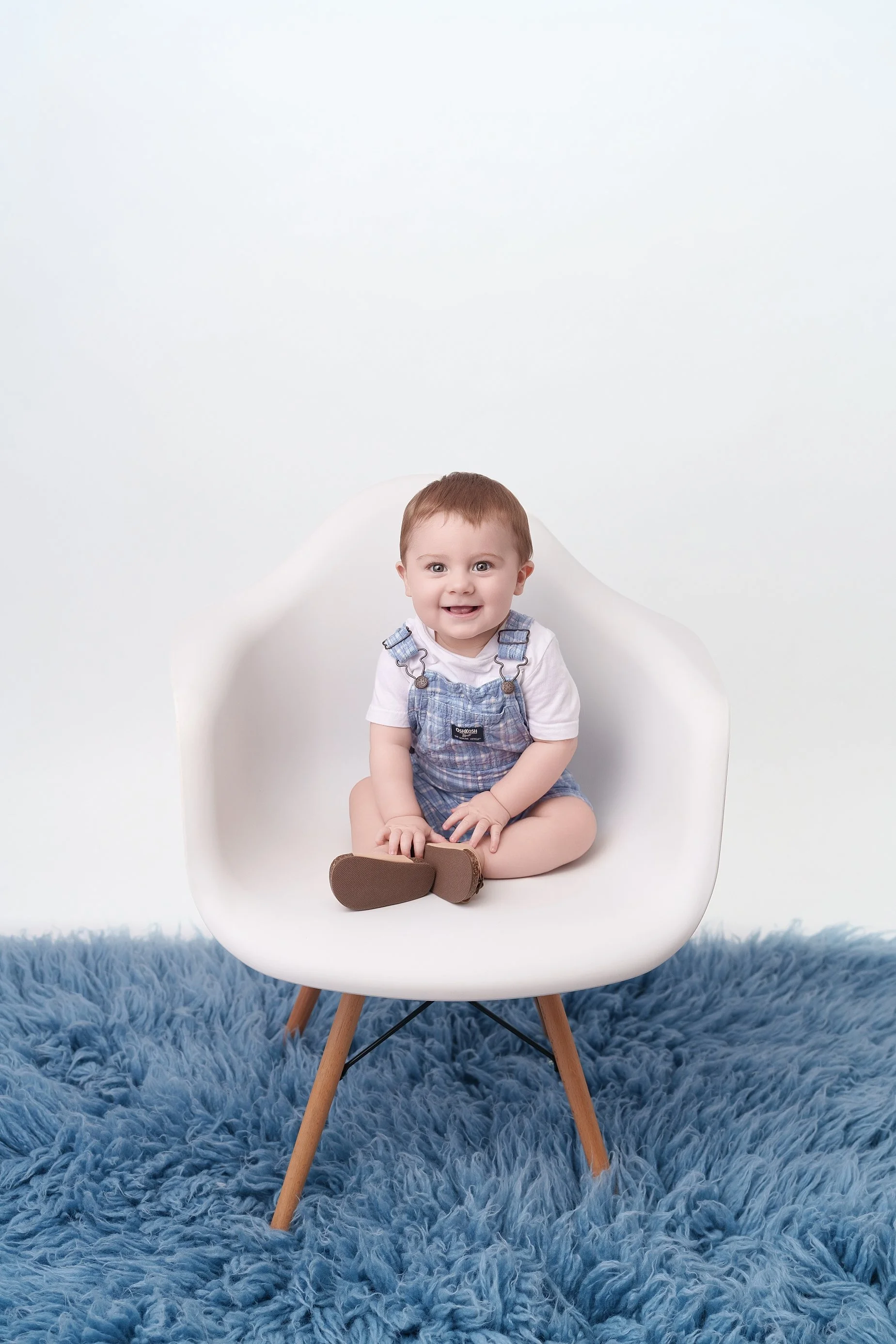 Smiling 9-month-old baby sitting on a modern white chair during a milestone photography session by Edwardsville baby photographer Conner James Photography.