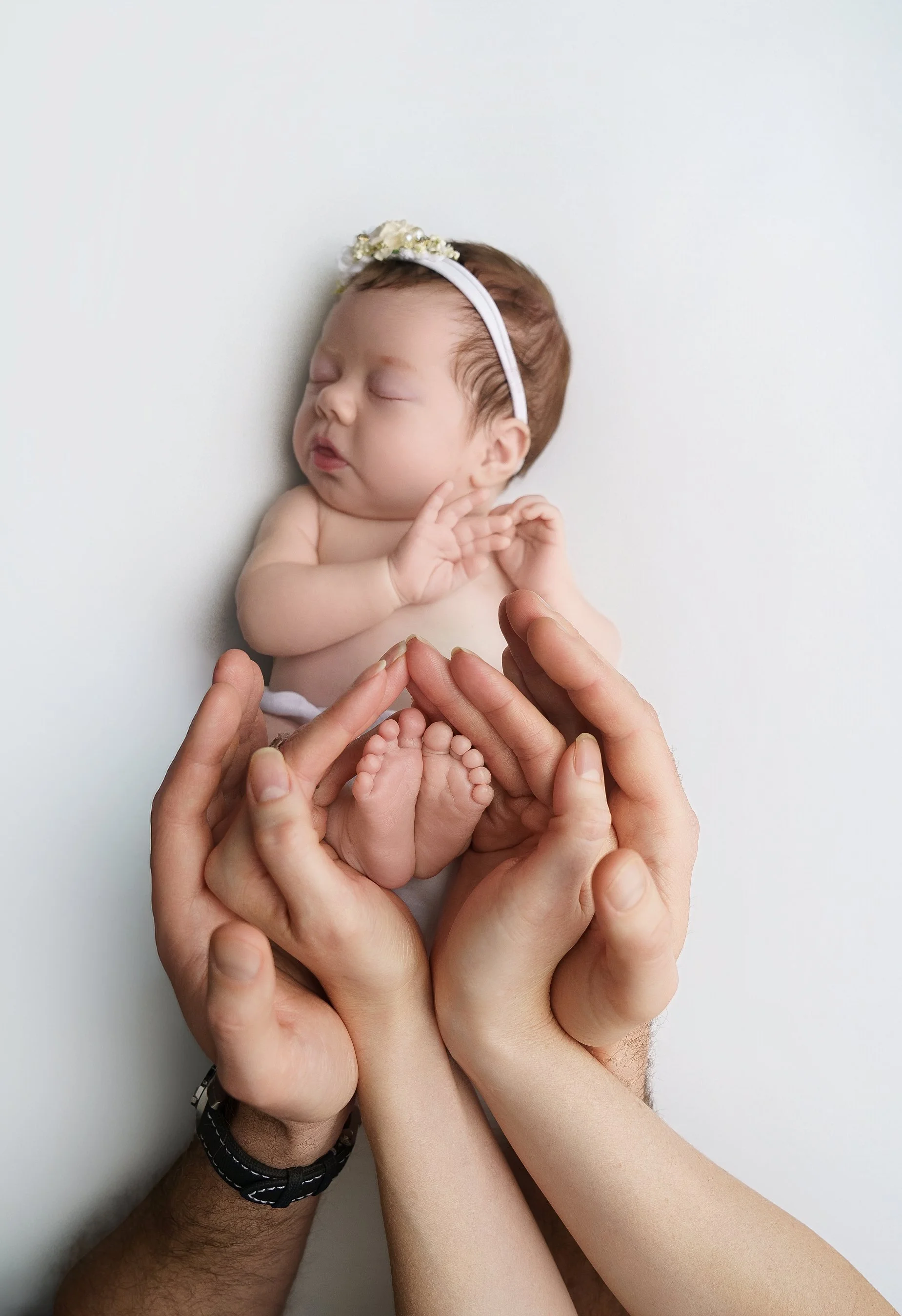 Newborn baby girl held safely in parents’ hands highlighting tiny feet and connection photographed in Metro East Illinois.