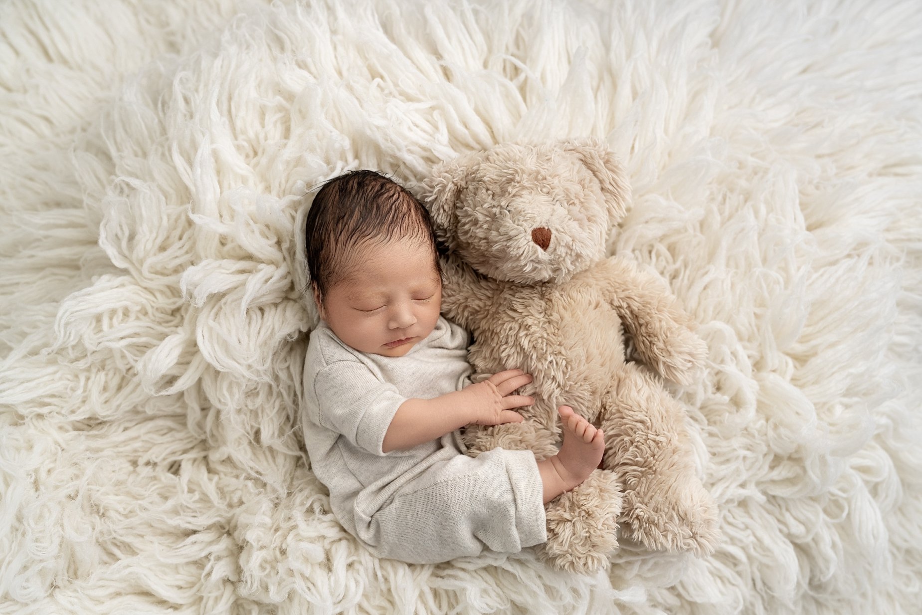 Newborn baby lying on soft cream blanket holding teddy bear in Glen Carbon Illinois studio