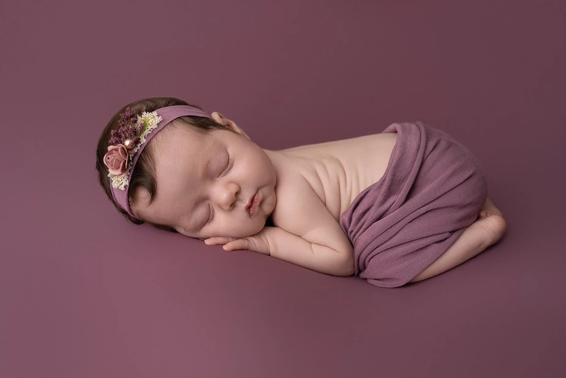 Sleeping newborn baby girl wrapped in mauve fabric photographed in Metro East Illinois studio
