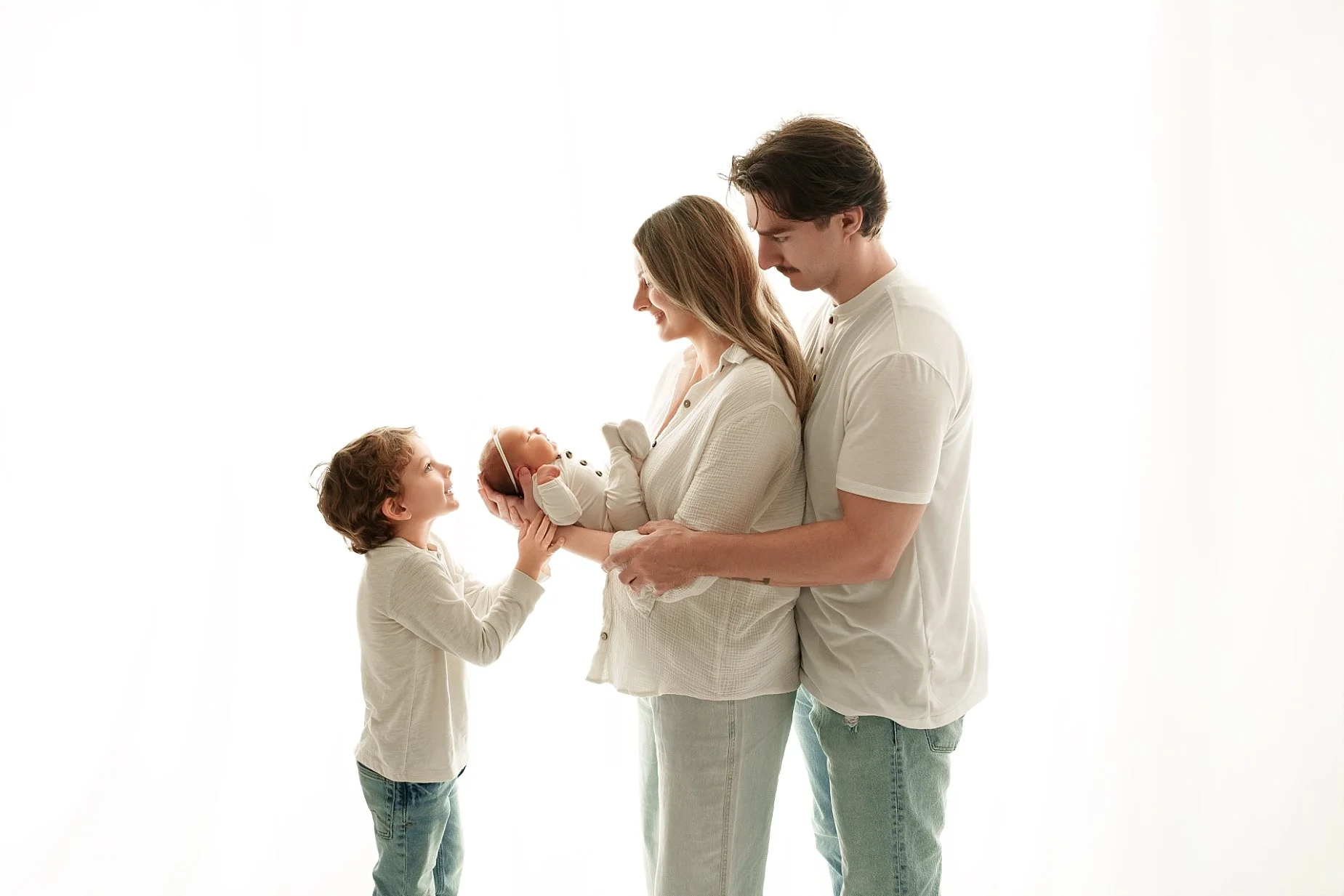 Big brother smiles at his newborn baby sister as their parents hold her during a family and sibling newborn photography session in Glen Carbon, Illinois, near Edwardsville.
