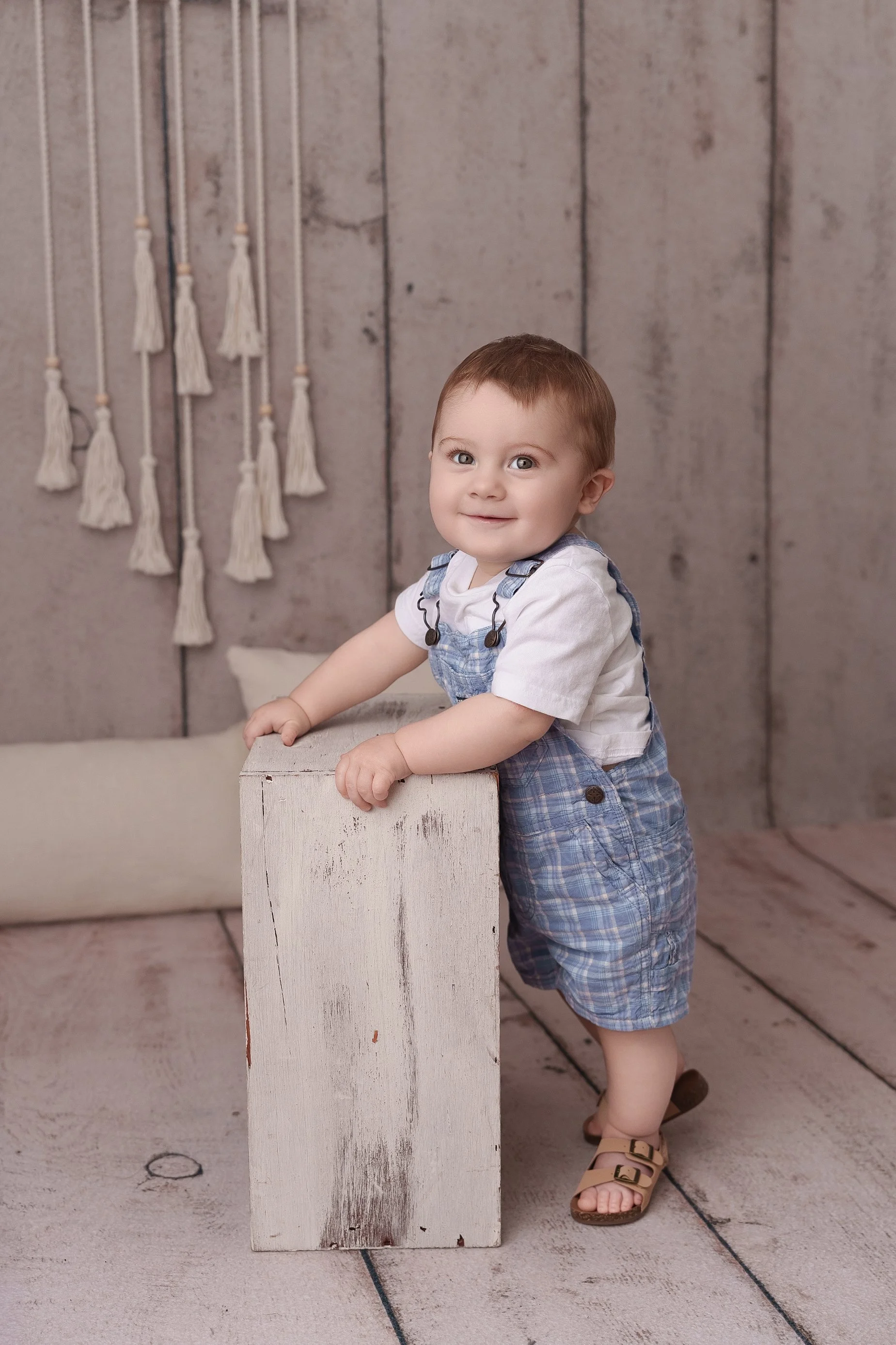 Happy 9-month-old baby standing while holding a rustic wooden block during a milestone photography session by Conner James Photography.
