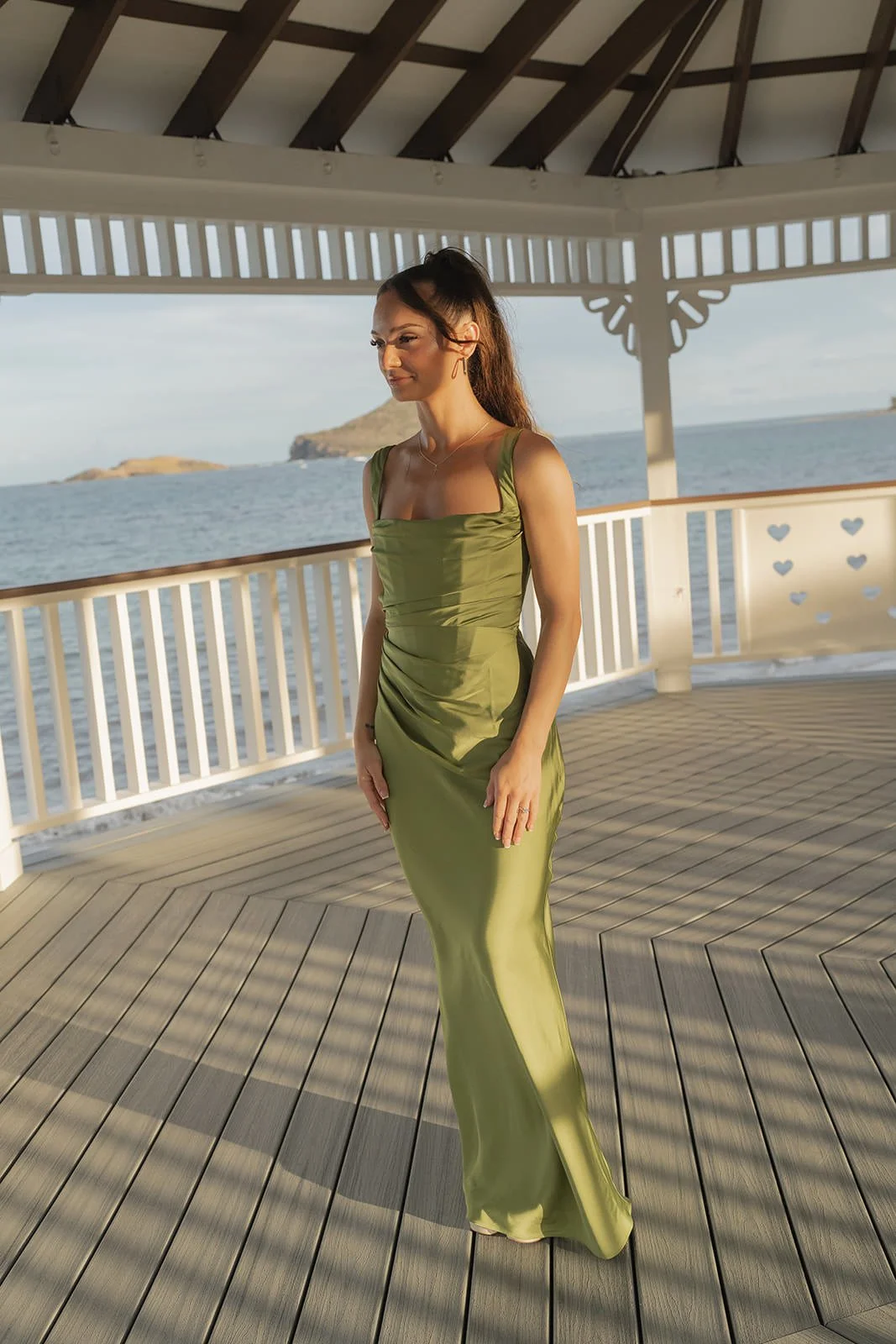 Bride in an olive green gown walking on a covered wooden deck at sunset, St. Lucia wedding weekend