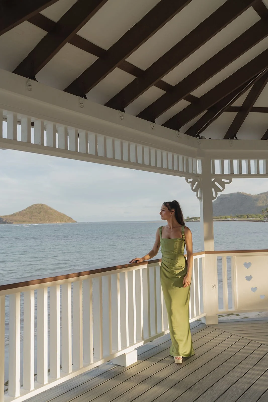 Bride in an olive green gown looking out over the water from a covered deck, St. Lucia destination wedding