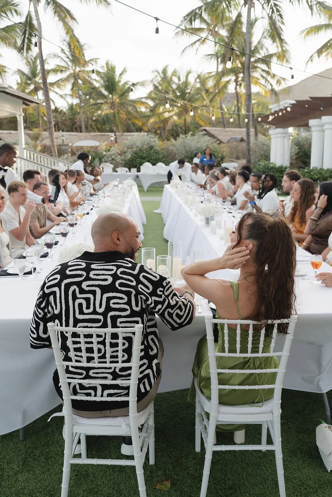 Wedding party seated at a long reception table with white florals and palm trees, St. Lucia